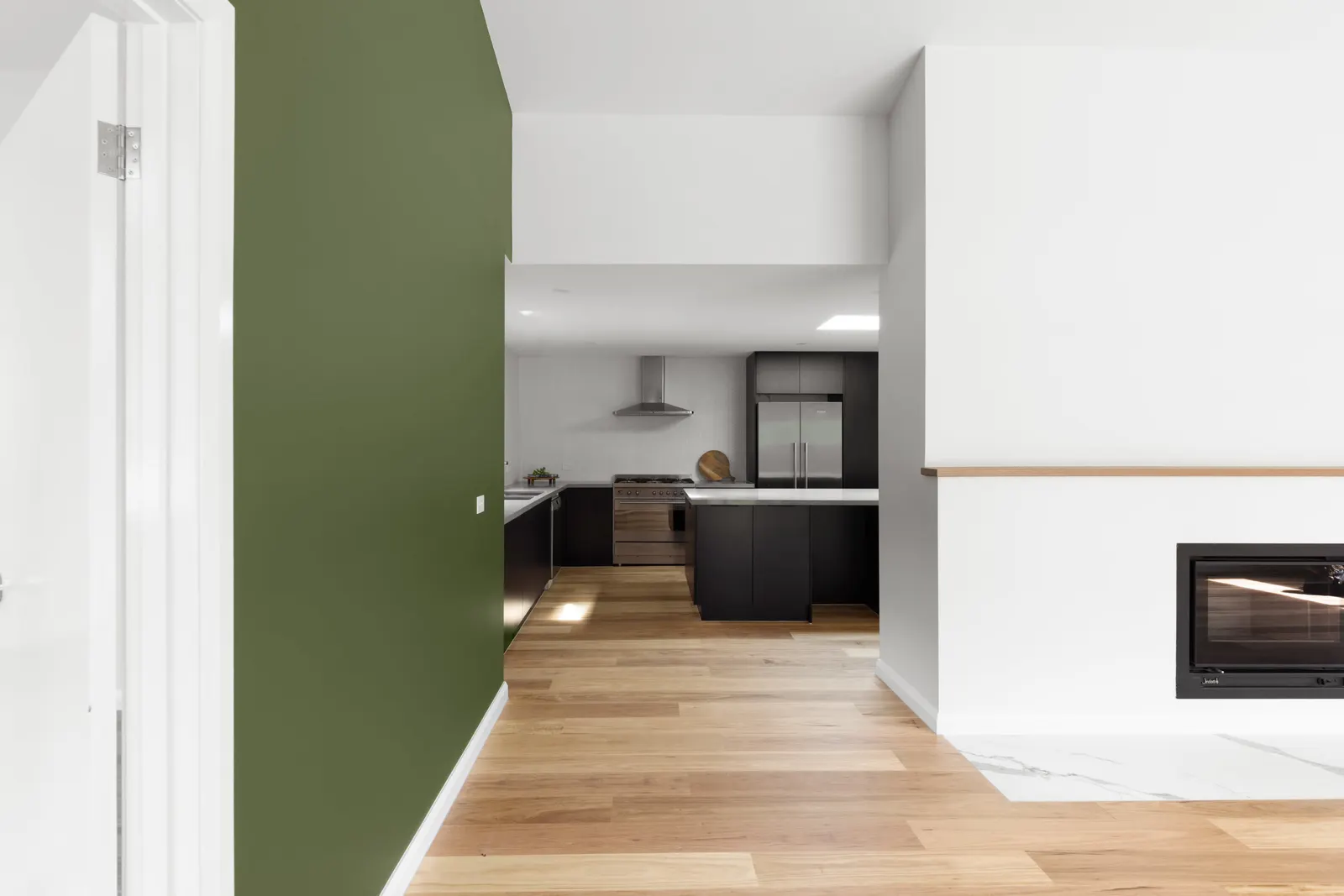 Green feature wall and rendered fireplace framing the kitchen and its stainless rangehood