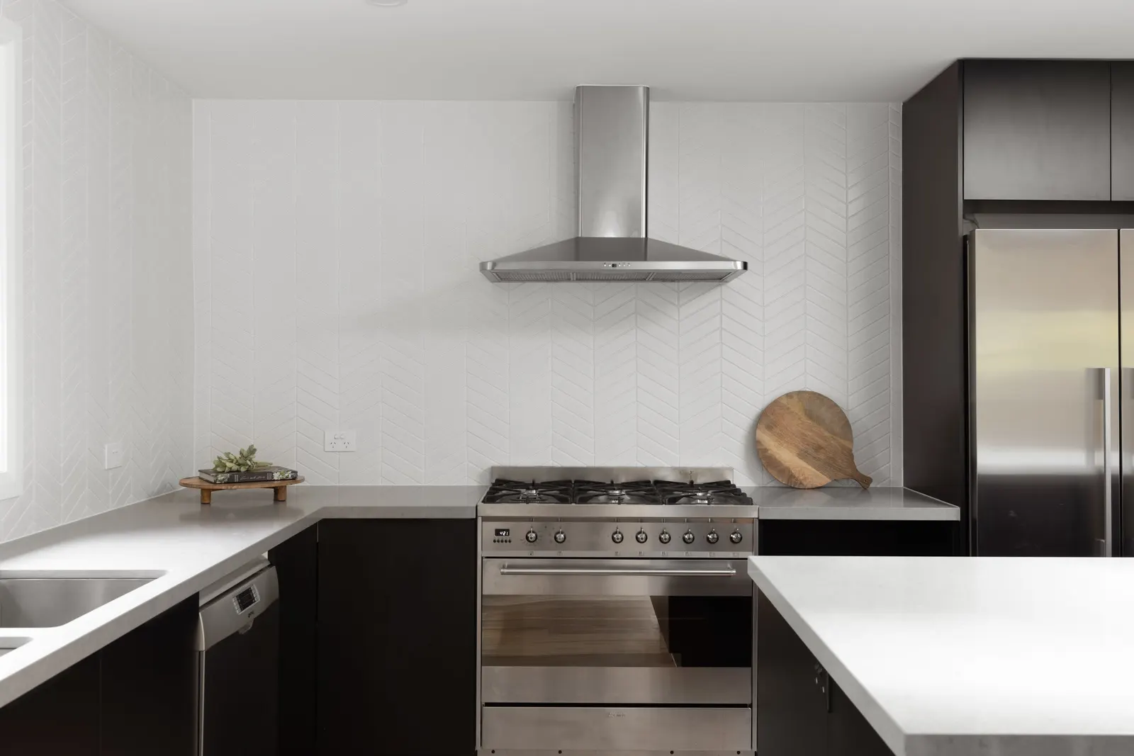 Stainless freestanding oven and rangehood between black joinery and pale stone benchtops