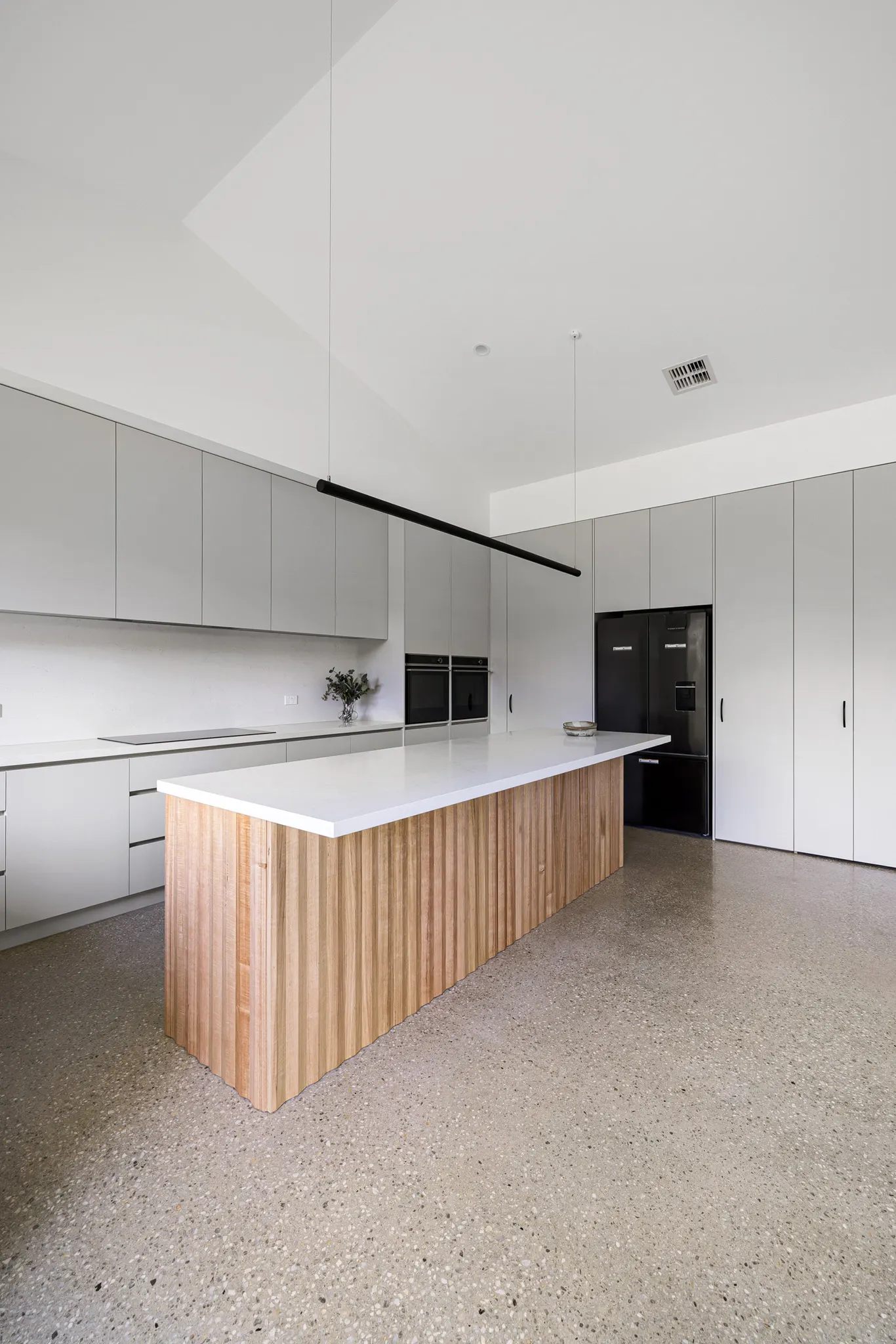 Stone-topped island beneath a raked ceiling, black linear pendant above pale grey joinery
