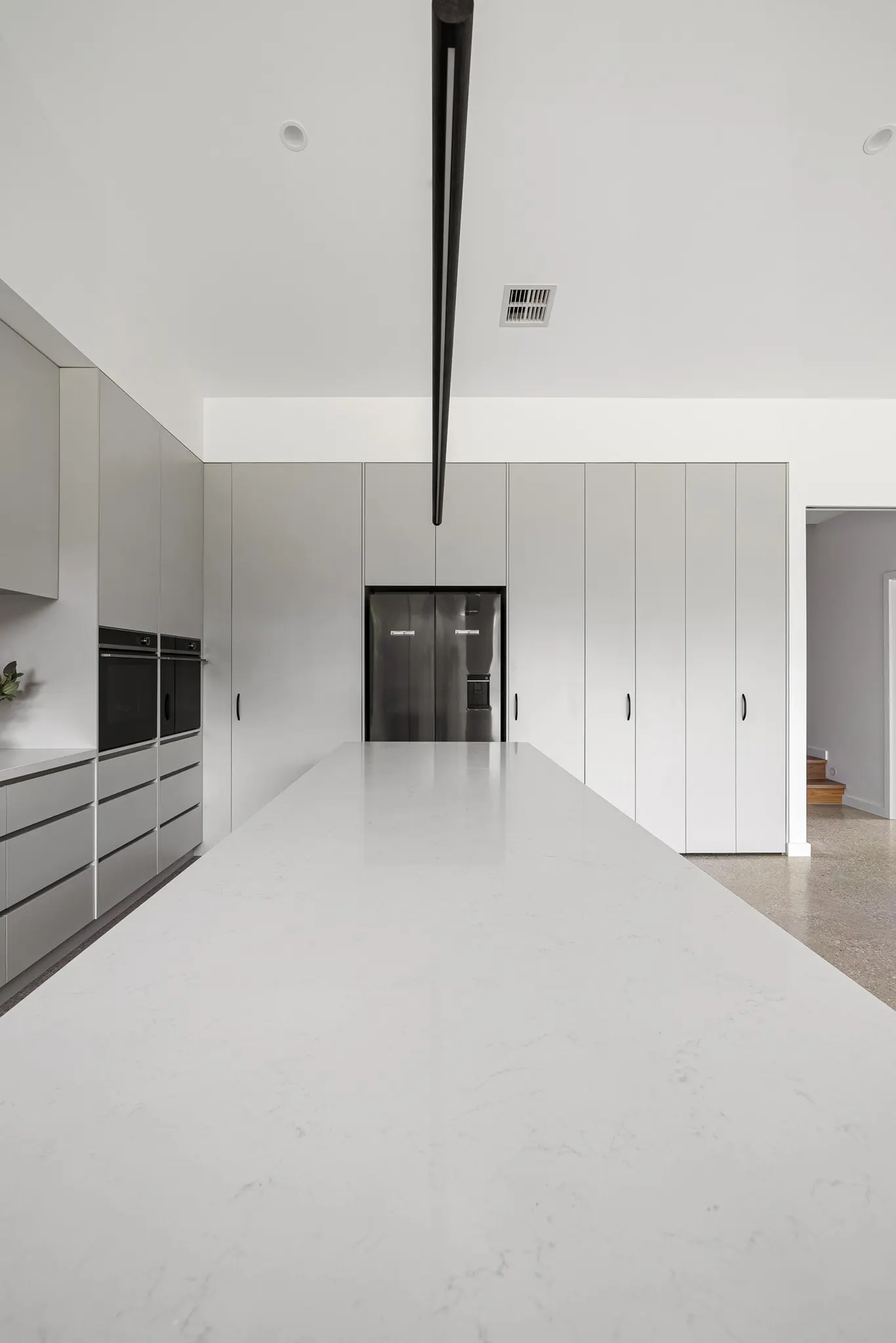 Looking along the white stone island to floor-to-ceiling pale grey joinery