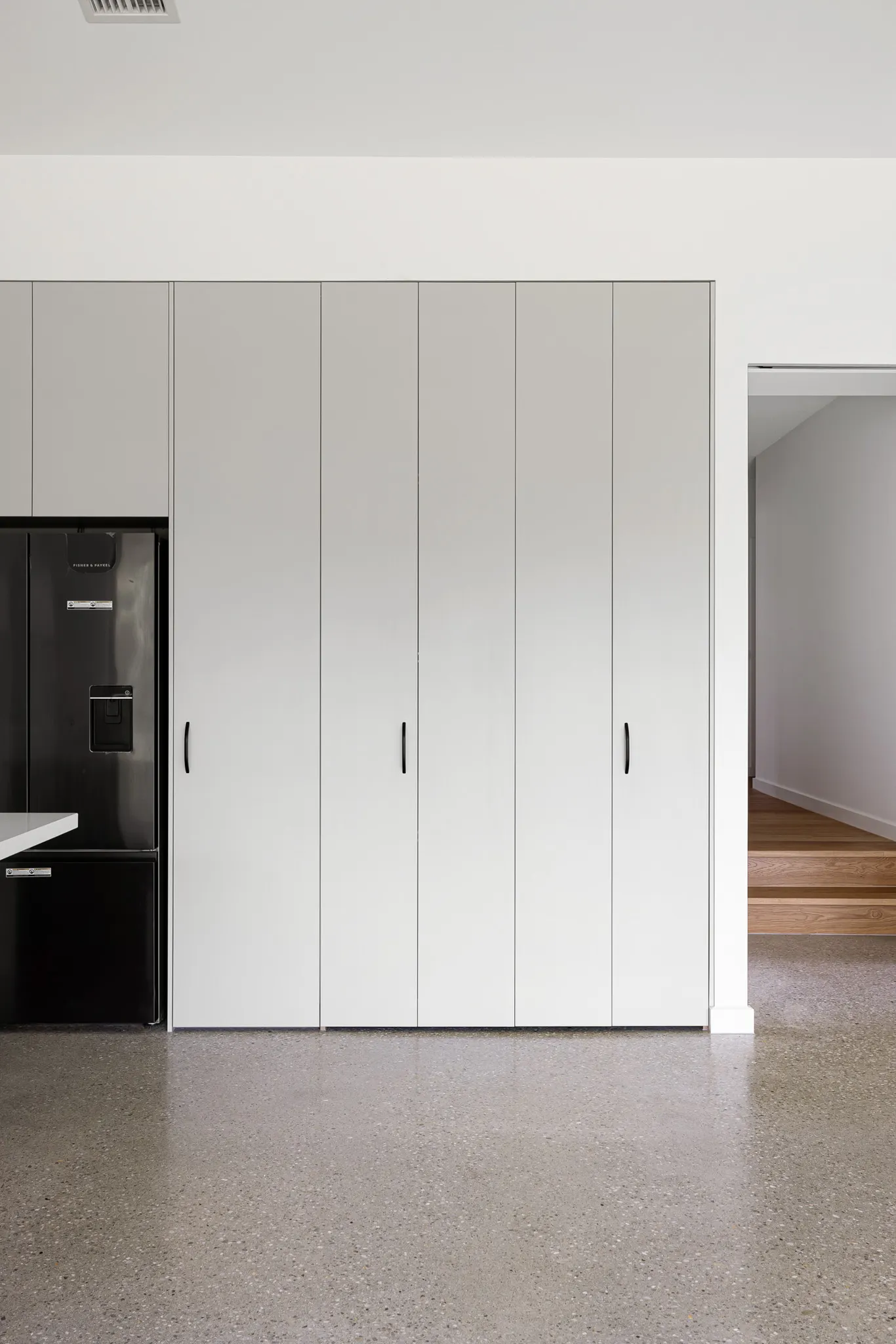 Floor-to-ceiling cupboard fronts with slim black handles above polished concrete