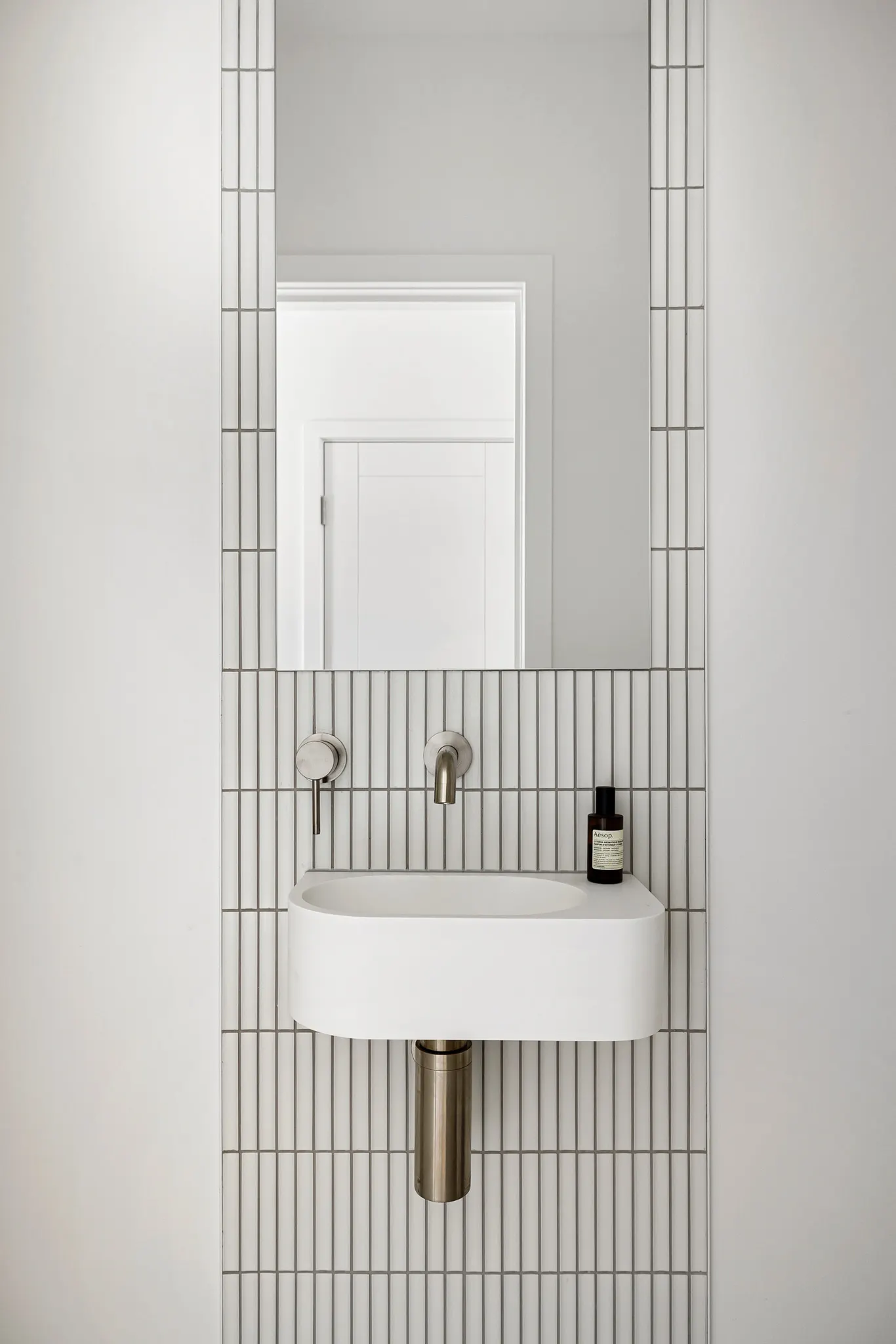 Powder room with a white finger-tile wall, wall-hung basin and brushed tapware