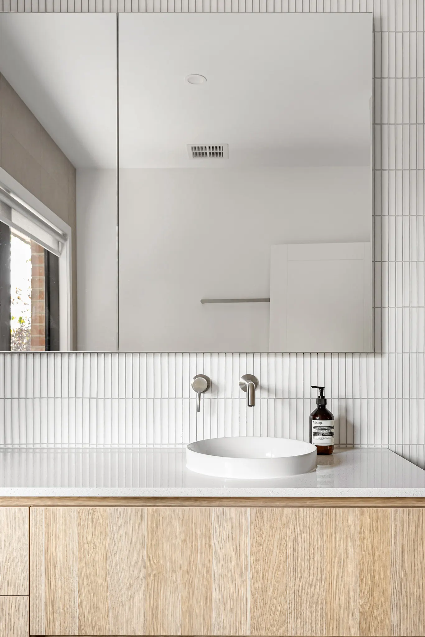 Above-counter basin on a timber vanity, white finger-tile splashback and mirrored cabinet