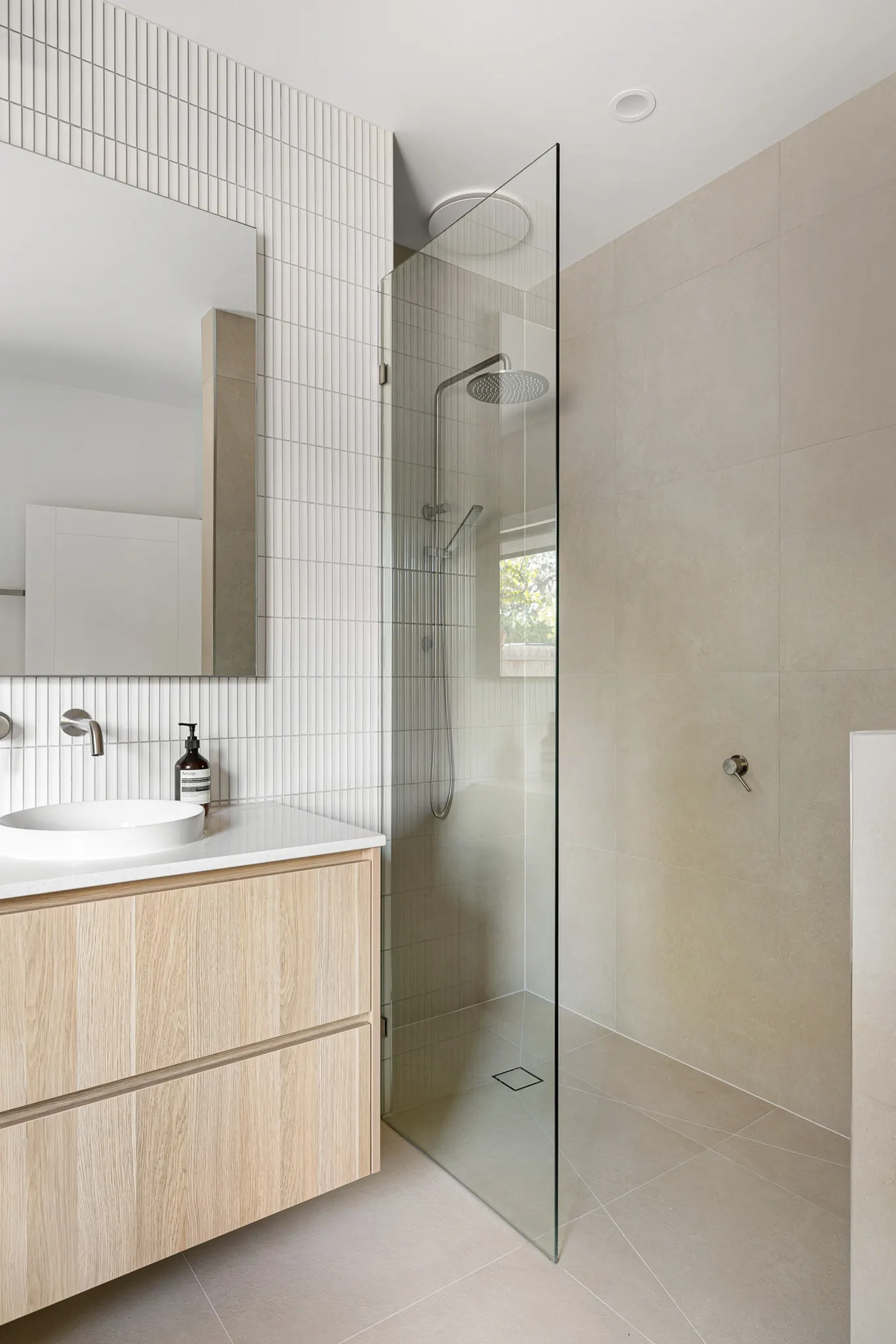 Walk-in shower behind frameless glass with a rain head, beside a timber vanity