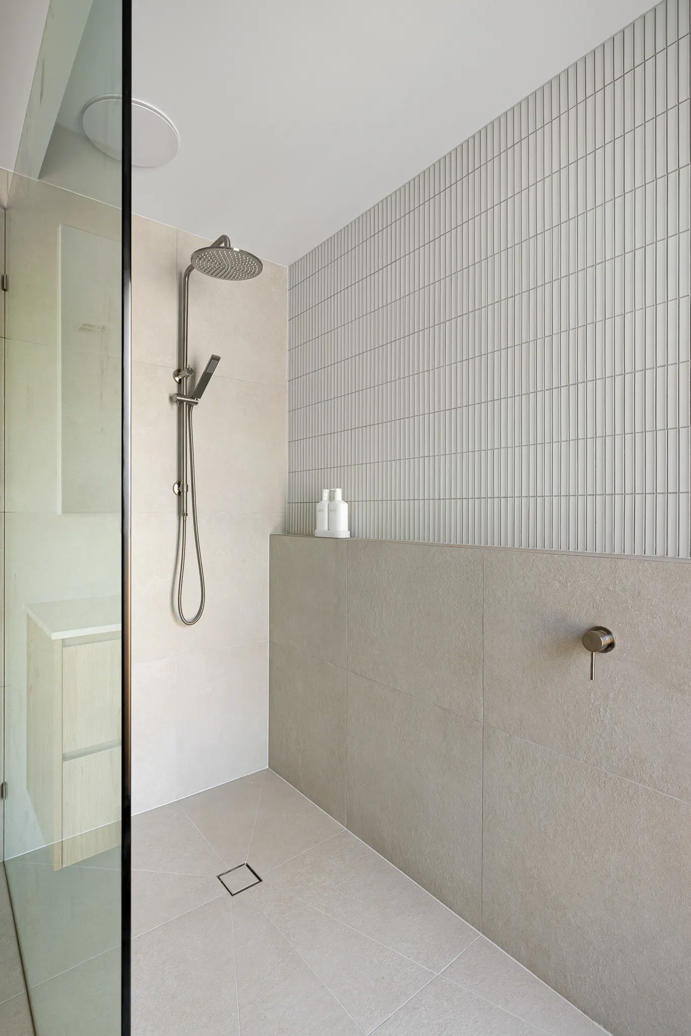 Shower recess with fluted upper tiles, rain head and hand shower over a square floor waste