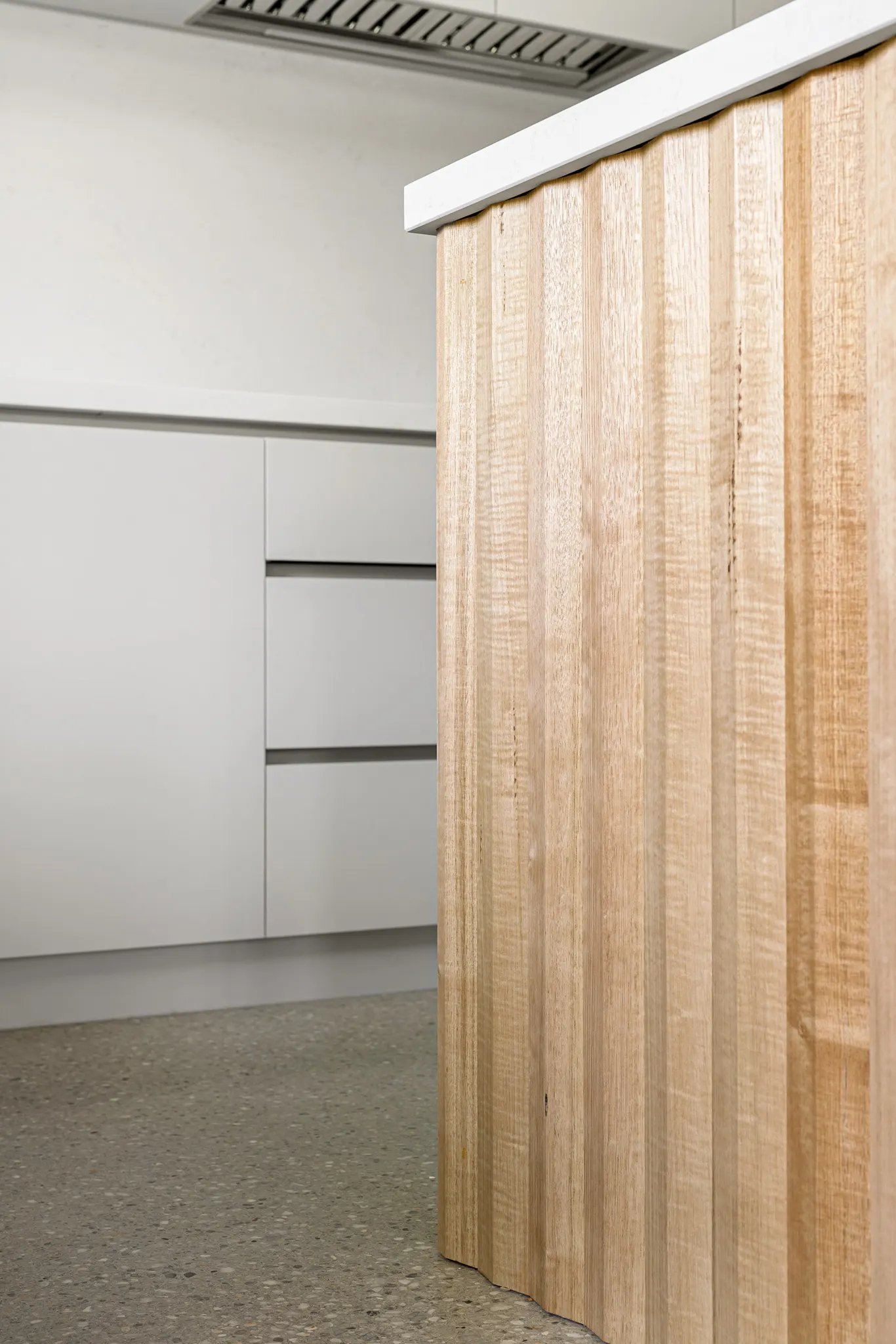 Detail of the fluted timber island end meeting the white stone benchtop overhang