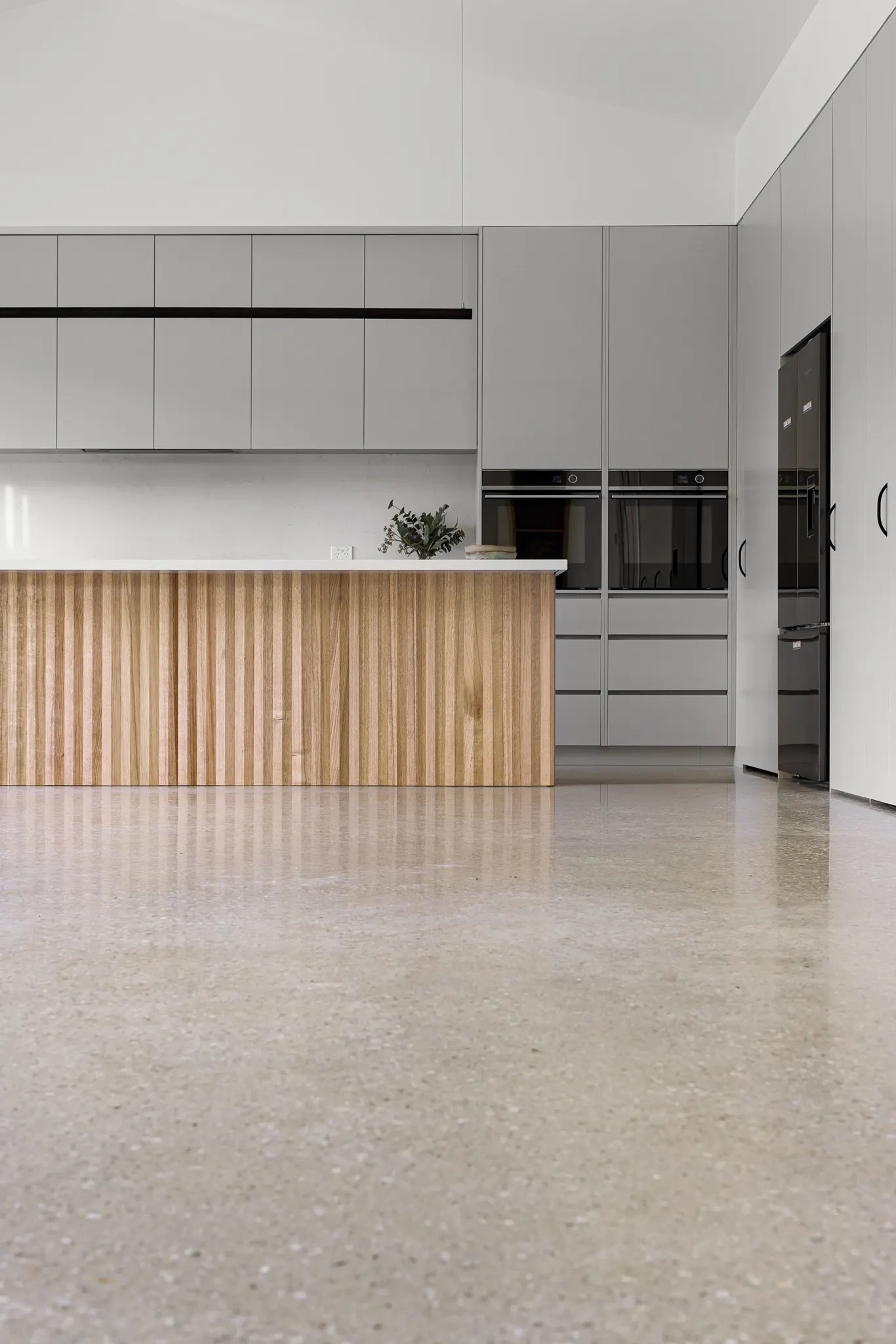 Low view across the polished concrete floor to the island and wall ovens