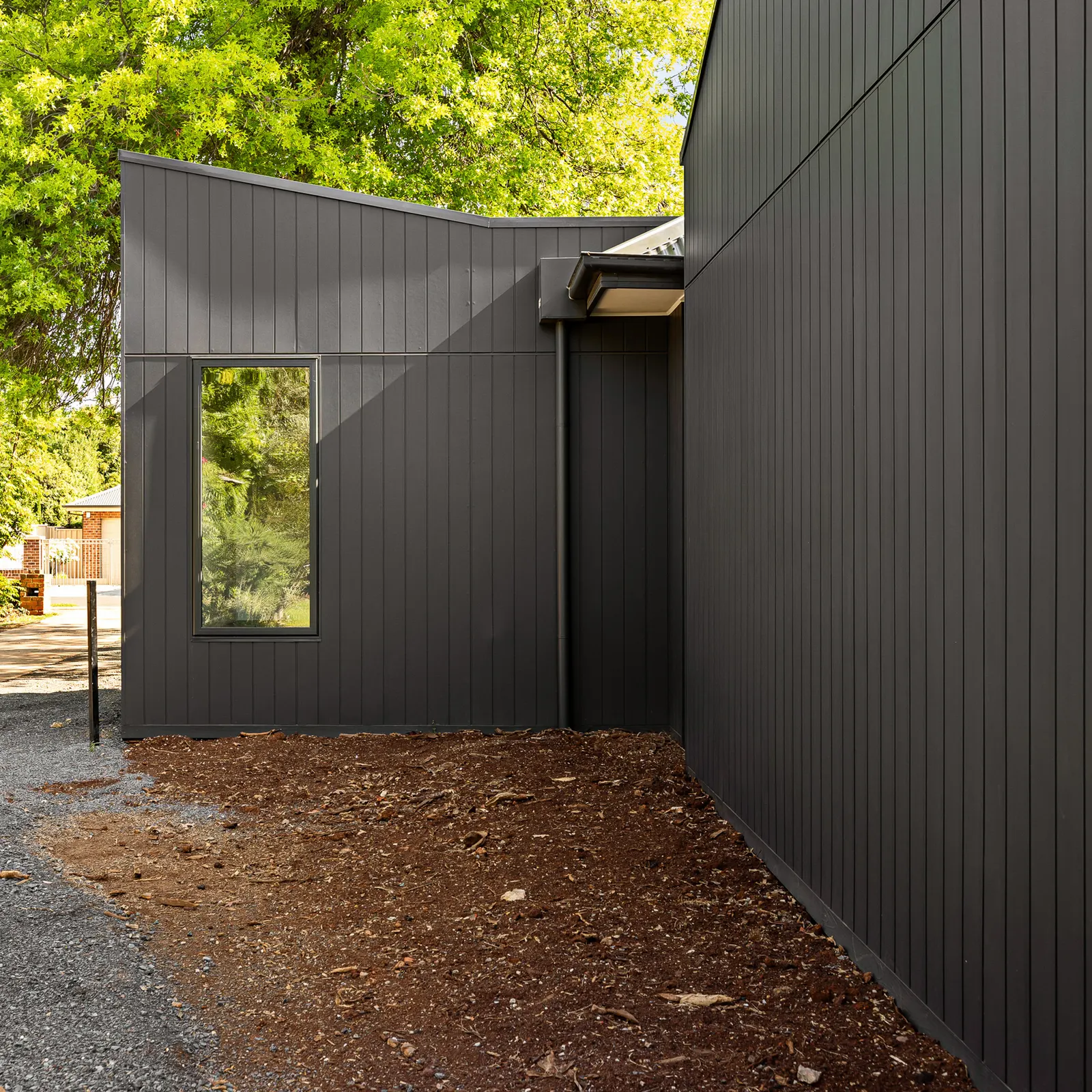 Dark vertical cladding meeting at an external corner above a freshly mulched garden bed