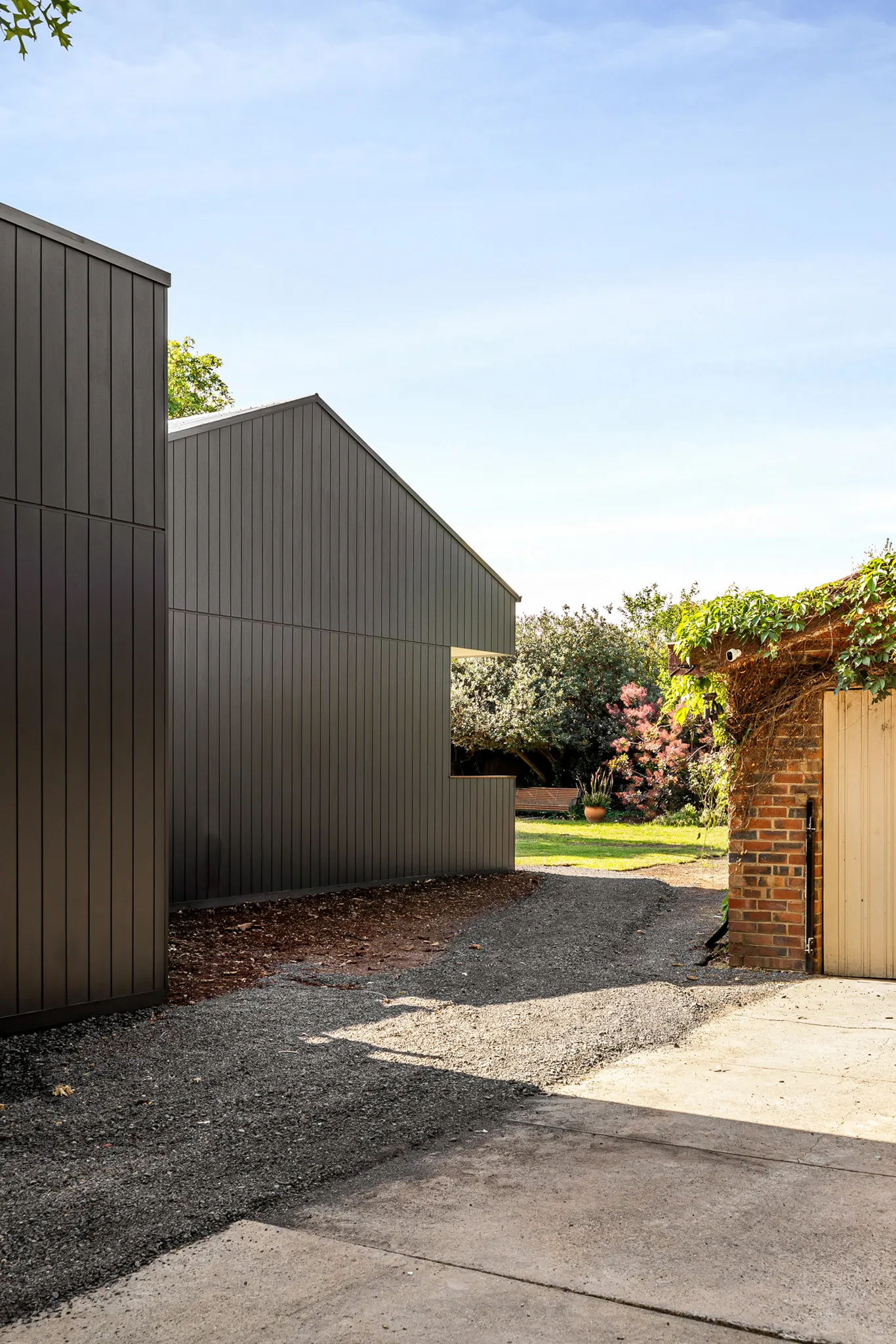 Gravel path between the dark gabled wing and an old red brick wall with a timber gate