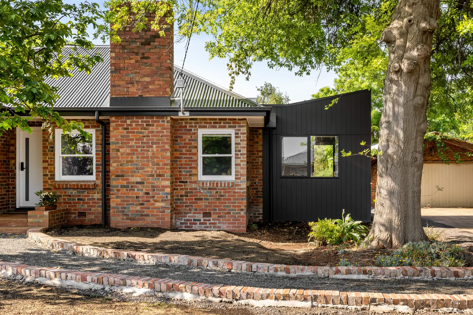 Red brick facade with chimney and corrugated roof alongside the dark-clad wing