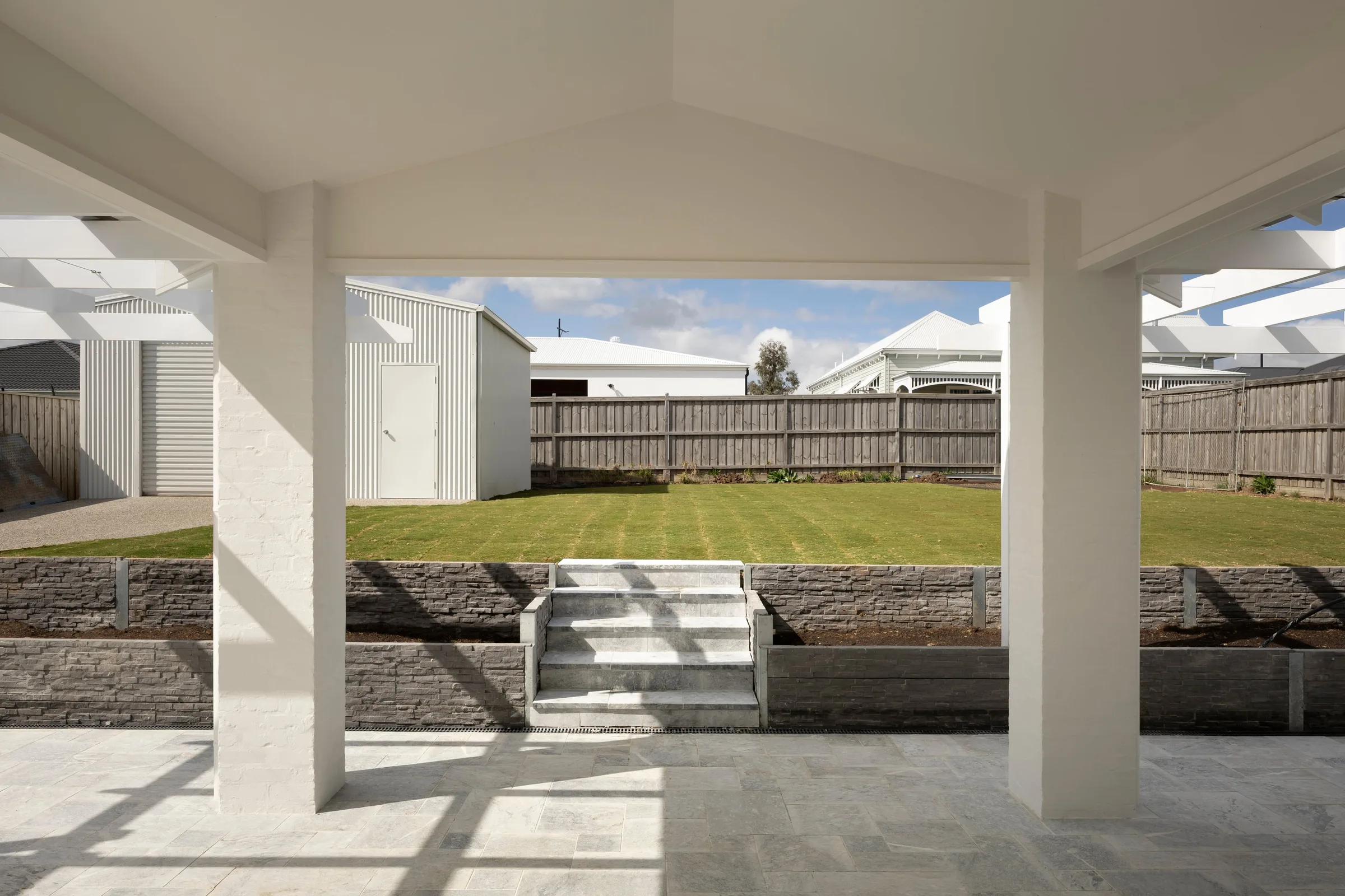 Alfresco under a gabled roof, looking over stone paving to the back lawn