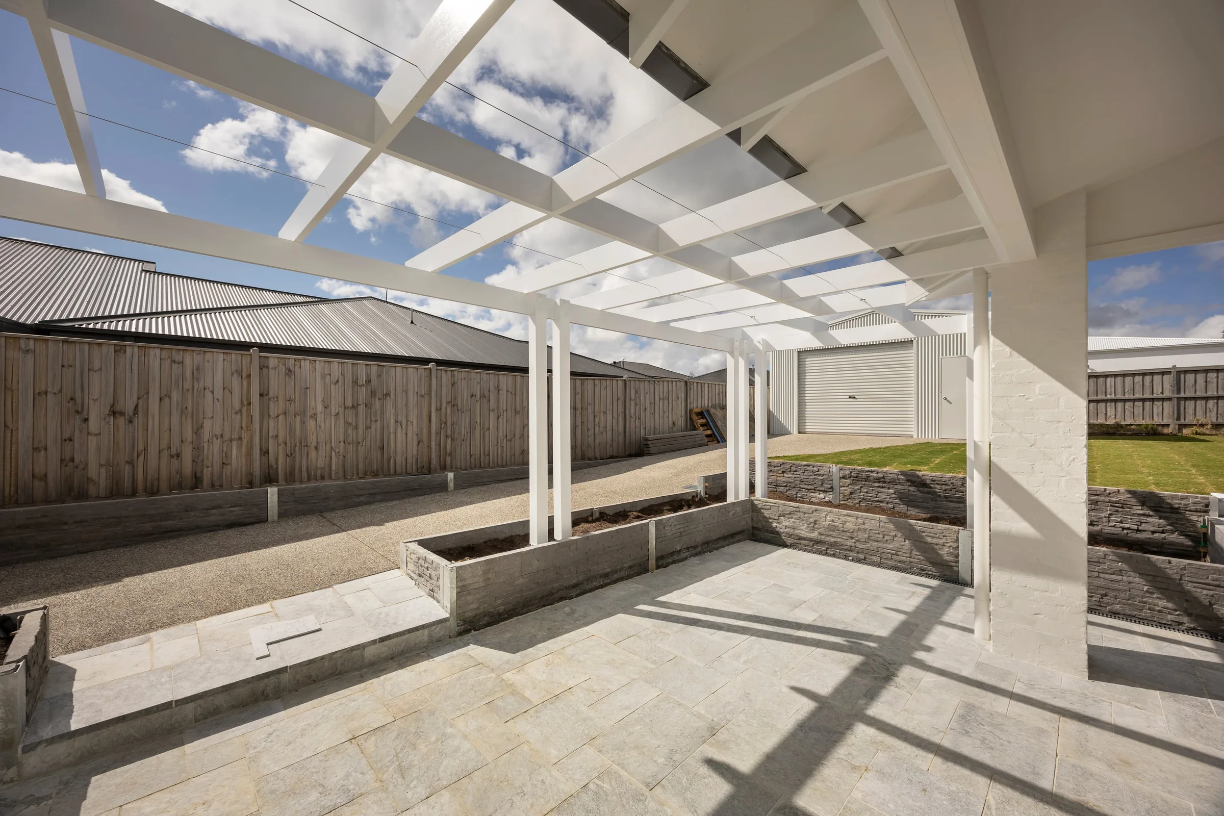 White timber pergola over stone paving and raised garden beds
