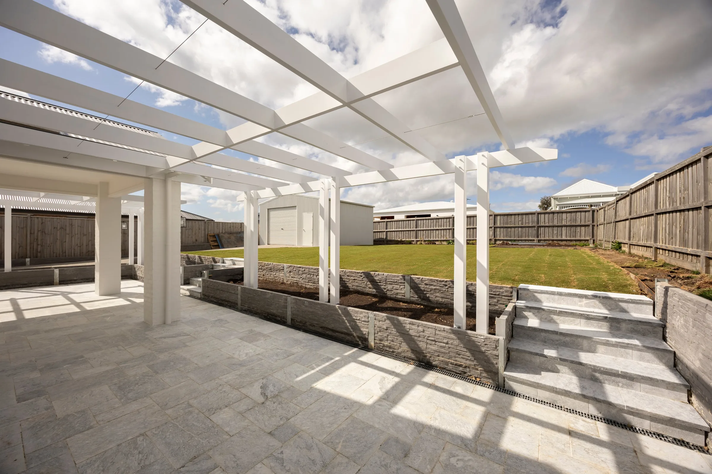 Pergola beams against the sky, with steps up to the back lawn
