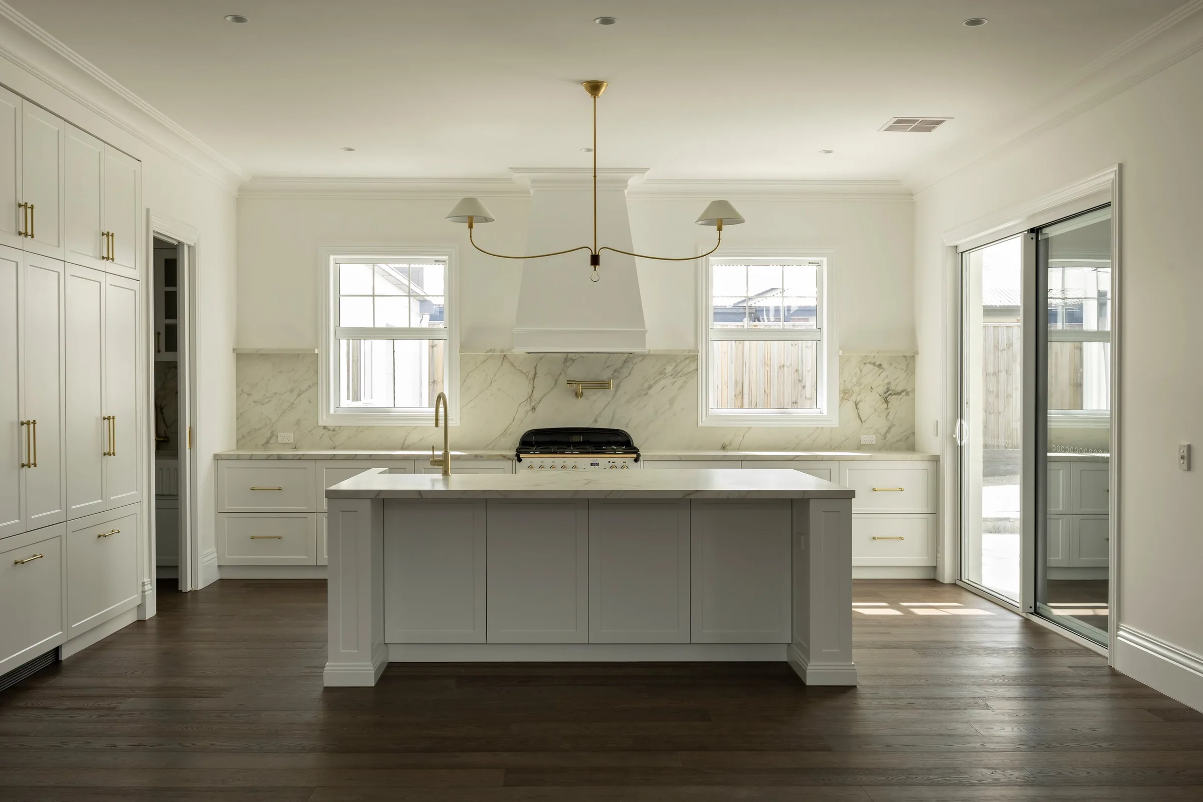 White kitchen with a panelled island, brass pendant and plaster range hood