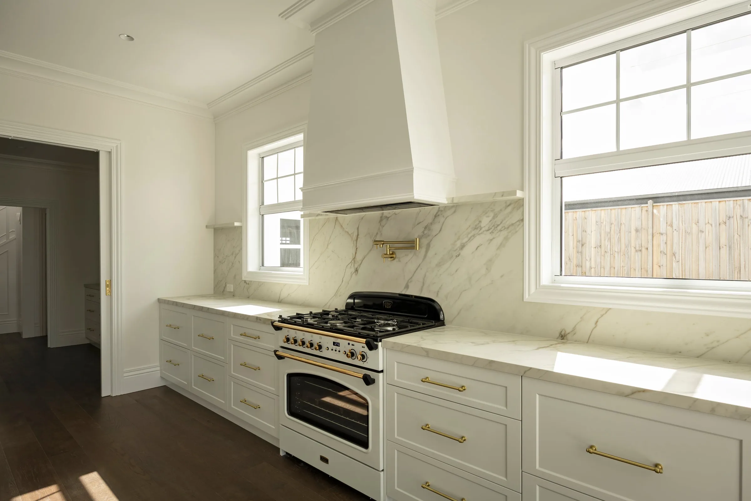 Black and cream freestanding cooker under the range hood, brass pot filler above
