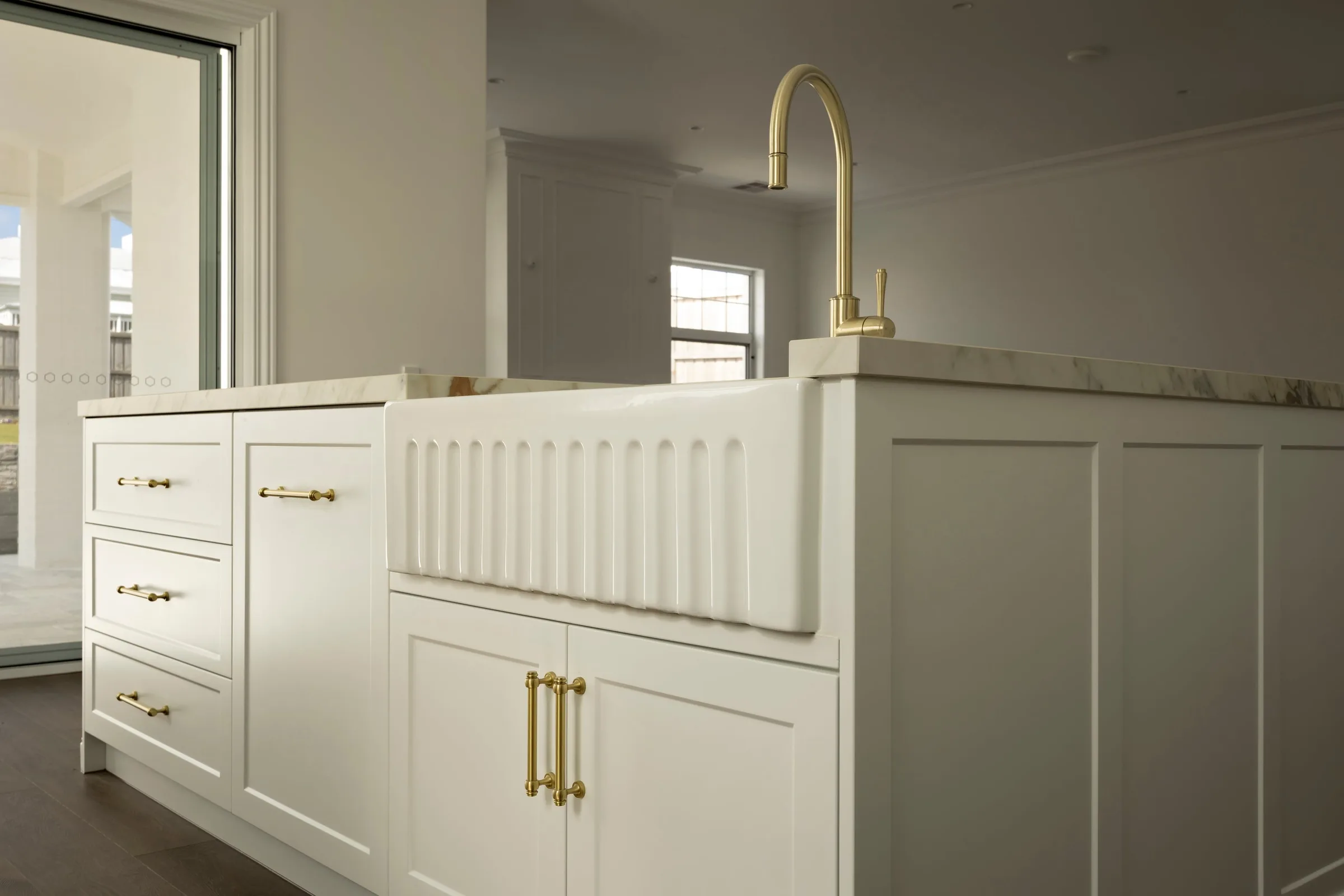 Fluted farmhouse sink and brass gooseneck tap set into the island