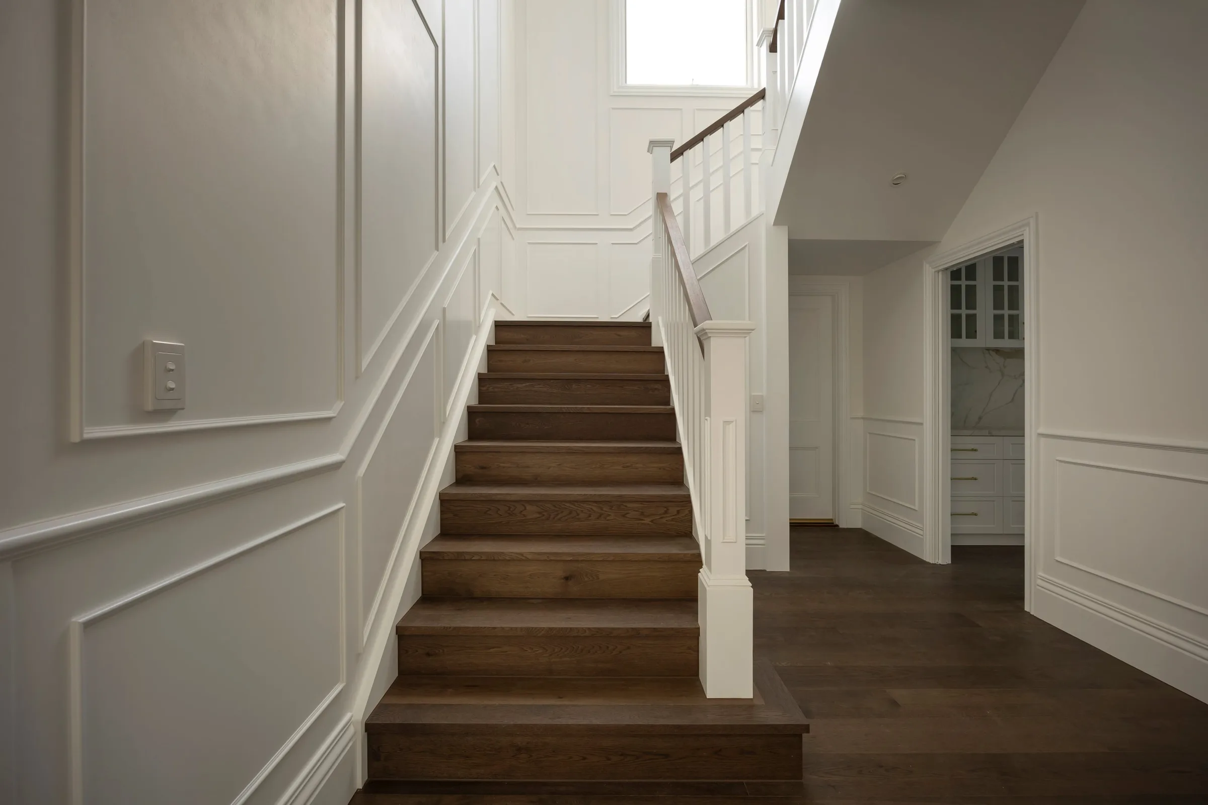 Oak staircase rising between panelled walls