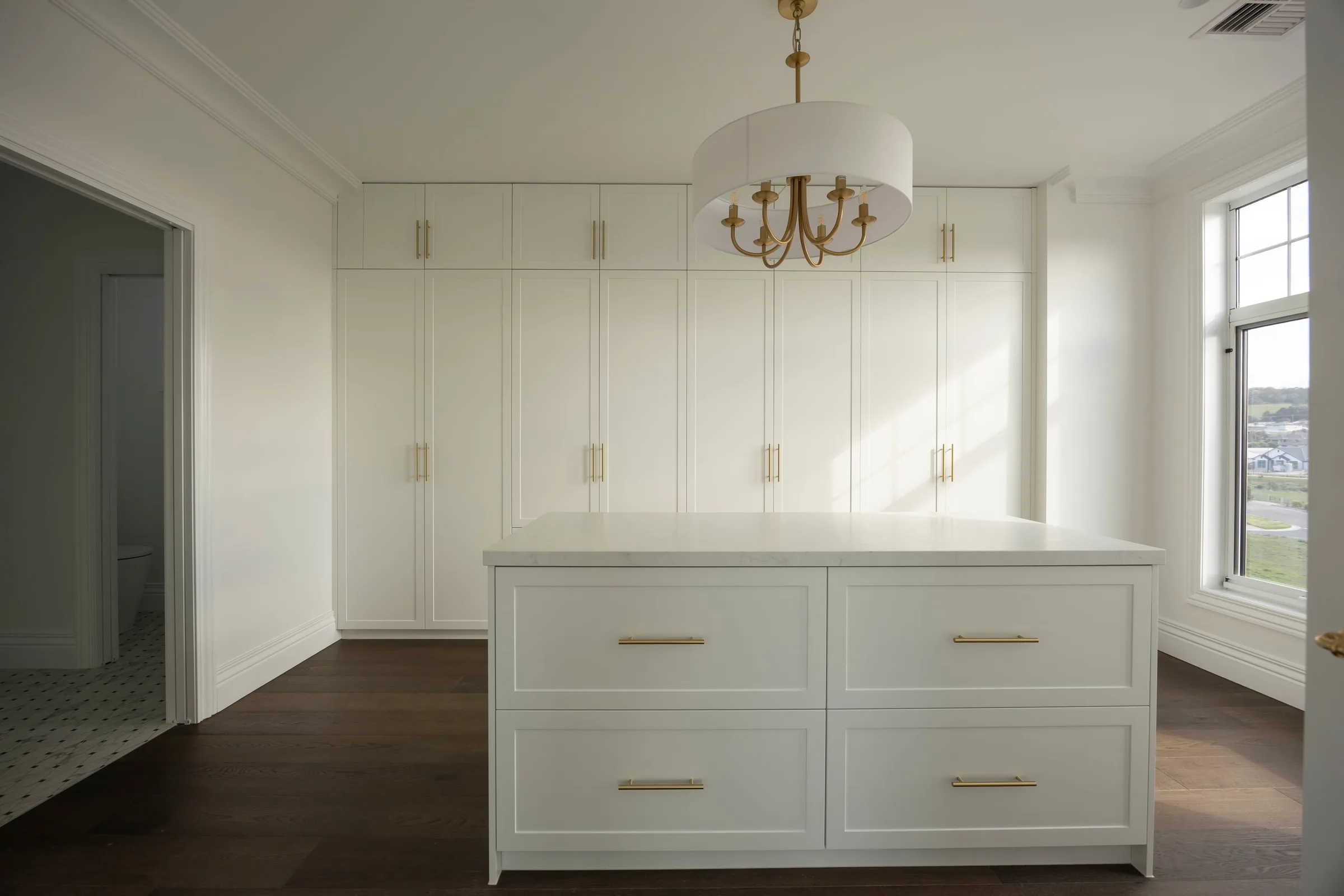 Walk-in robe with a drawer island under a drum chandelier