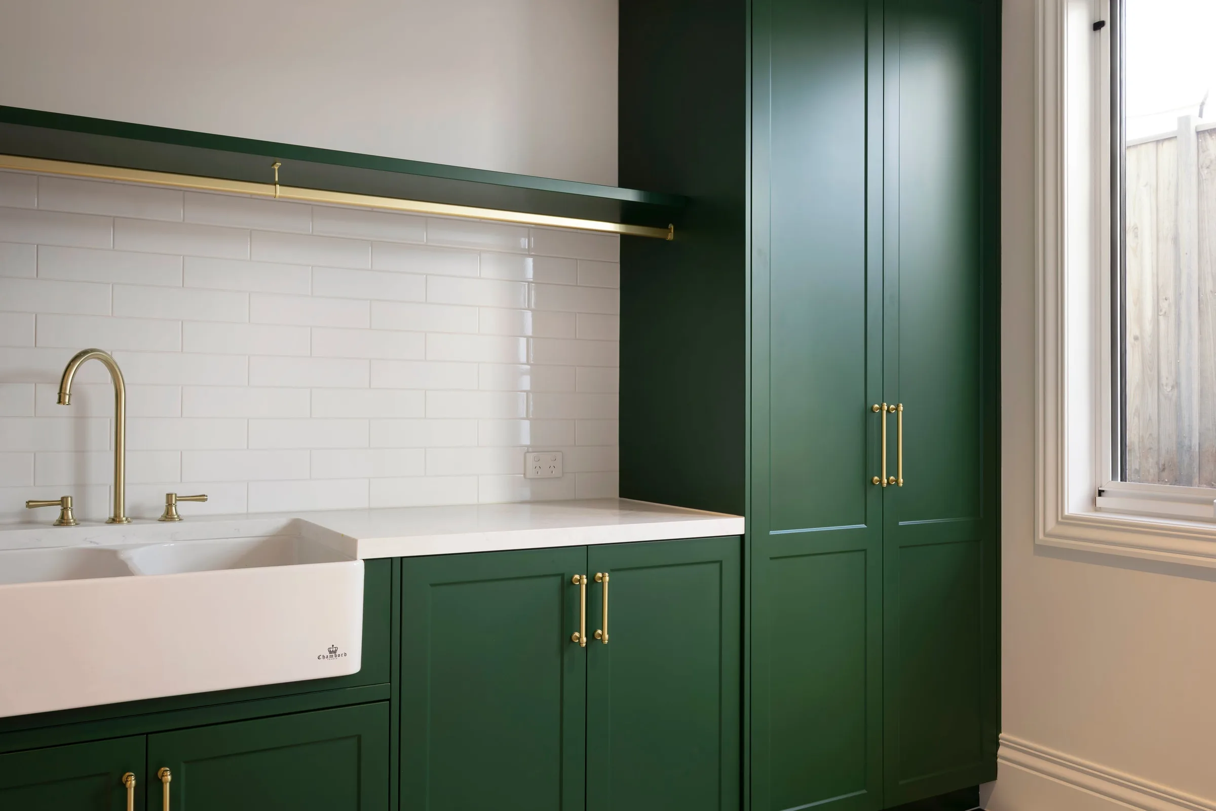 Farmhouse laundry sink and brass tap below a brass hanging rail
