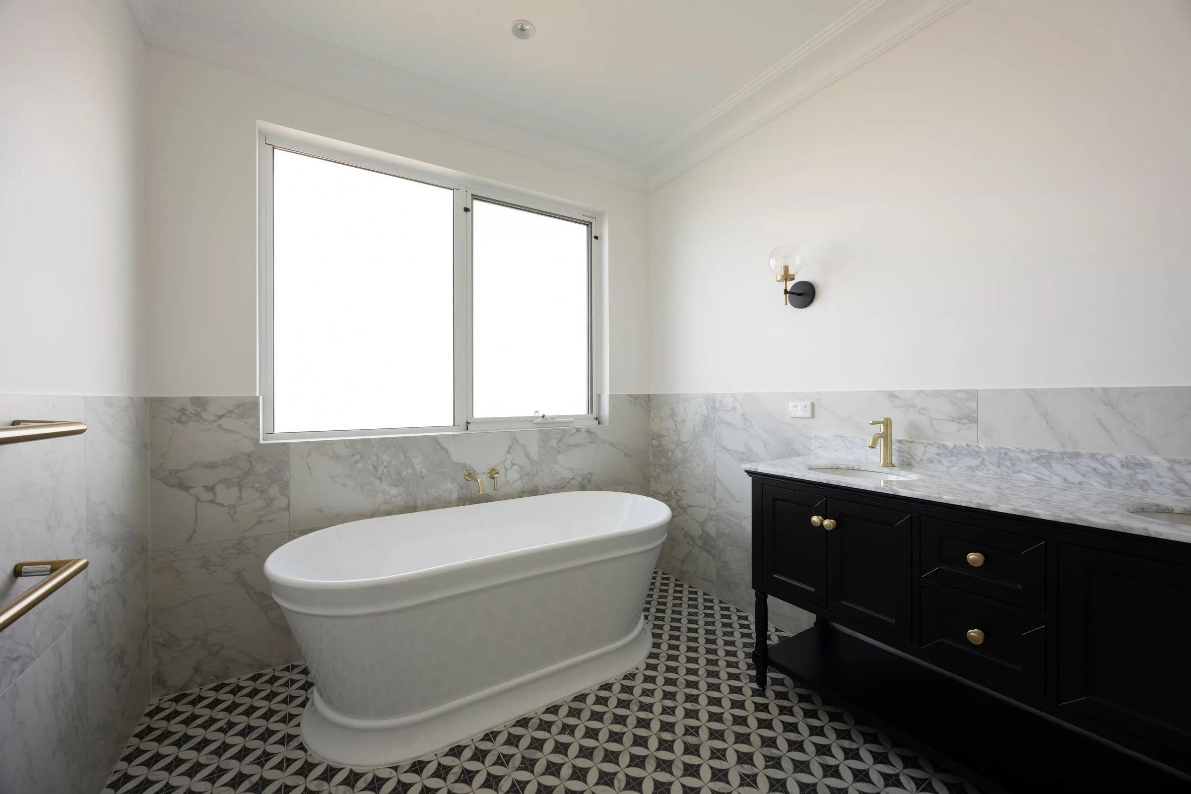Freestanding bath below a window, marble-look tiles to half height