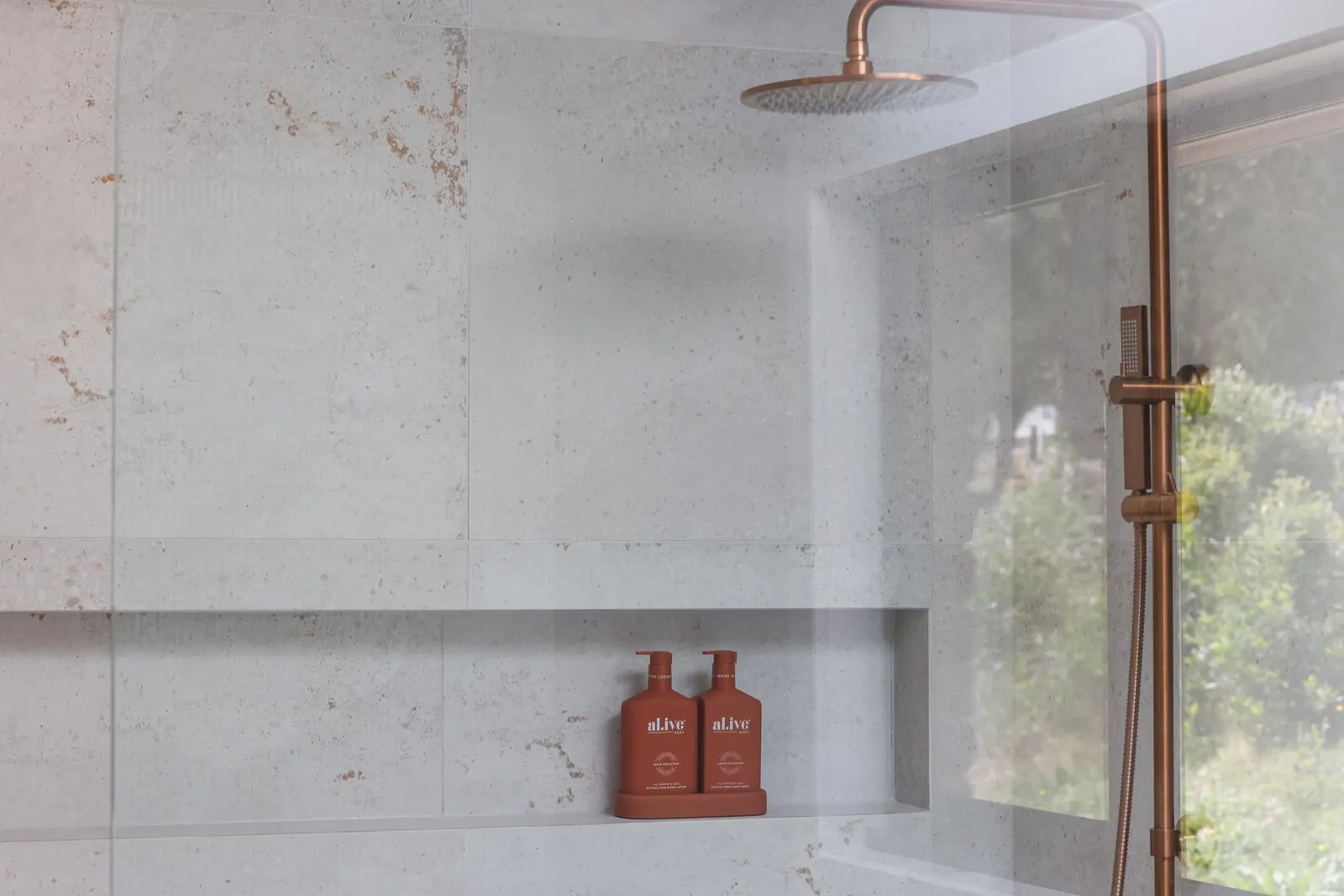 Brass rain shower and rail in a concrete-look tiled shower with a recessed niche
