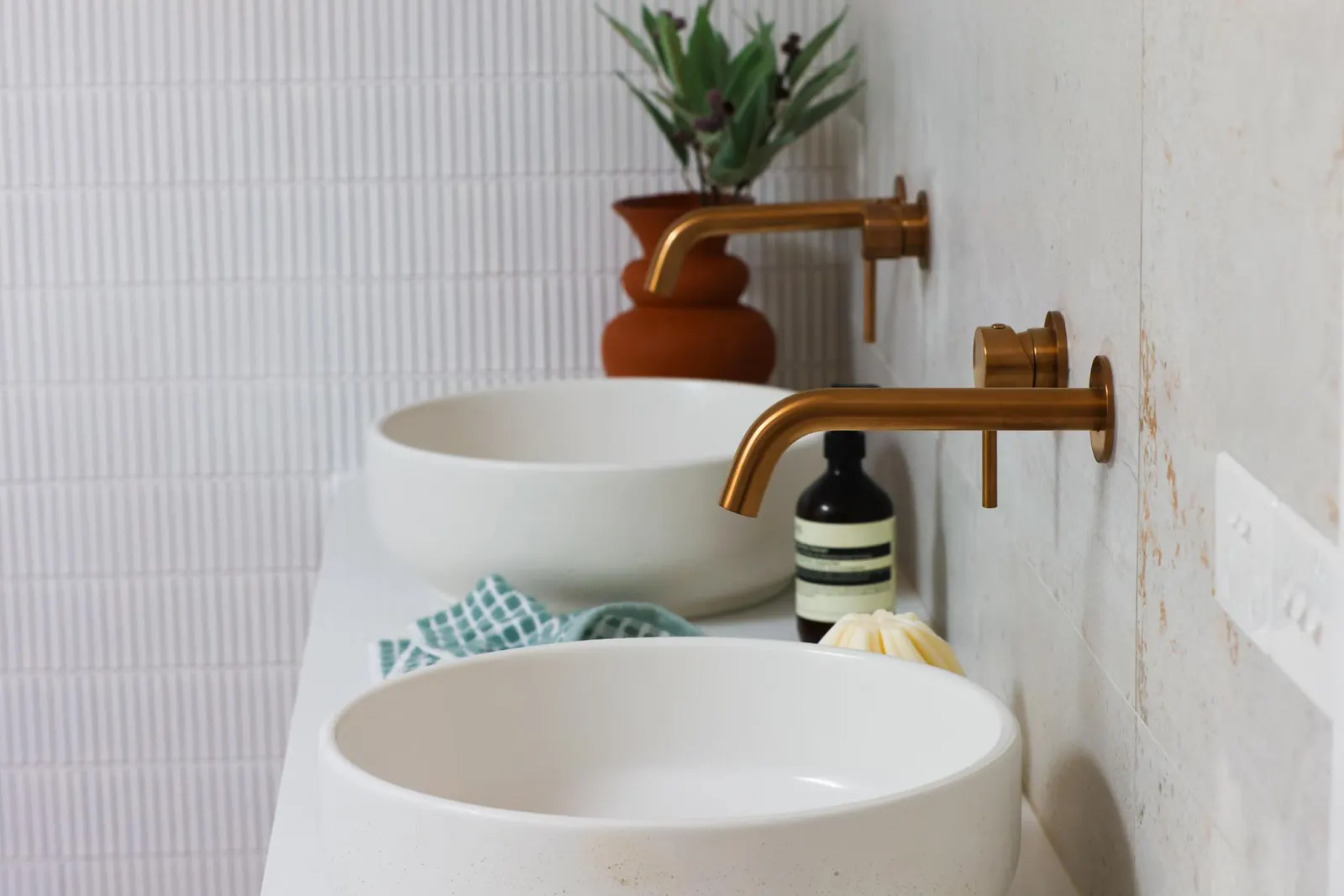 Two round white vessel basins with brass wall mixers against white mosaic tiling