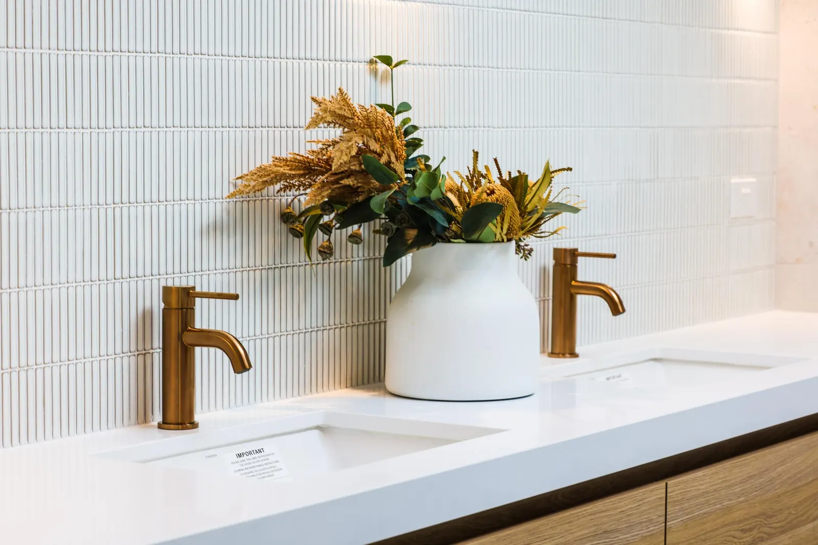 Twin undermount basins in a stone benchtop with brass tapware and dried native flowers