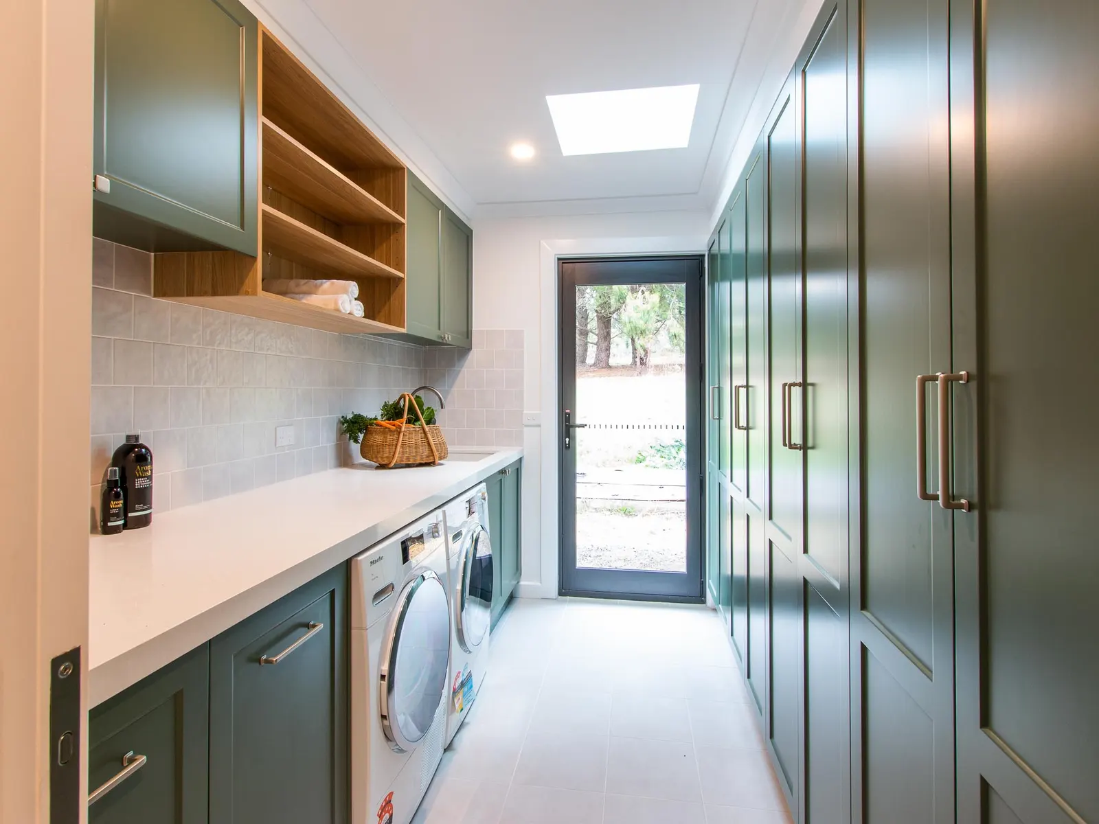 Galley laundry with green joinery, a front loader and a glazed door to the garden