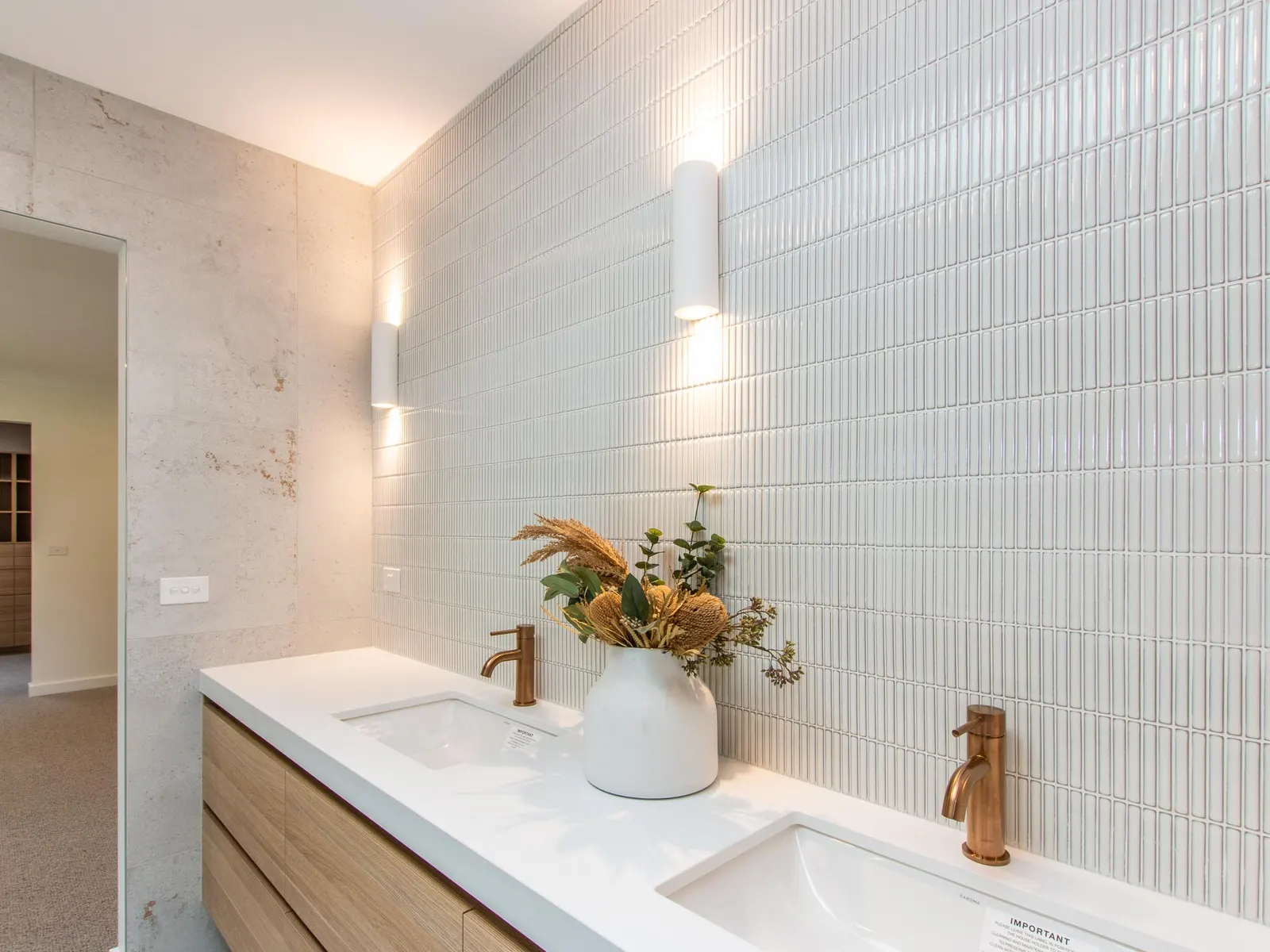 Ensuite vanity lit by wall sconces, with timber joinery and a marble-look wall return