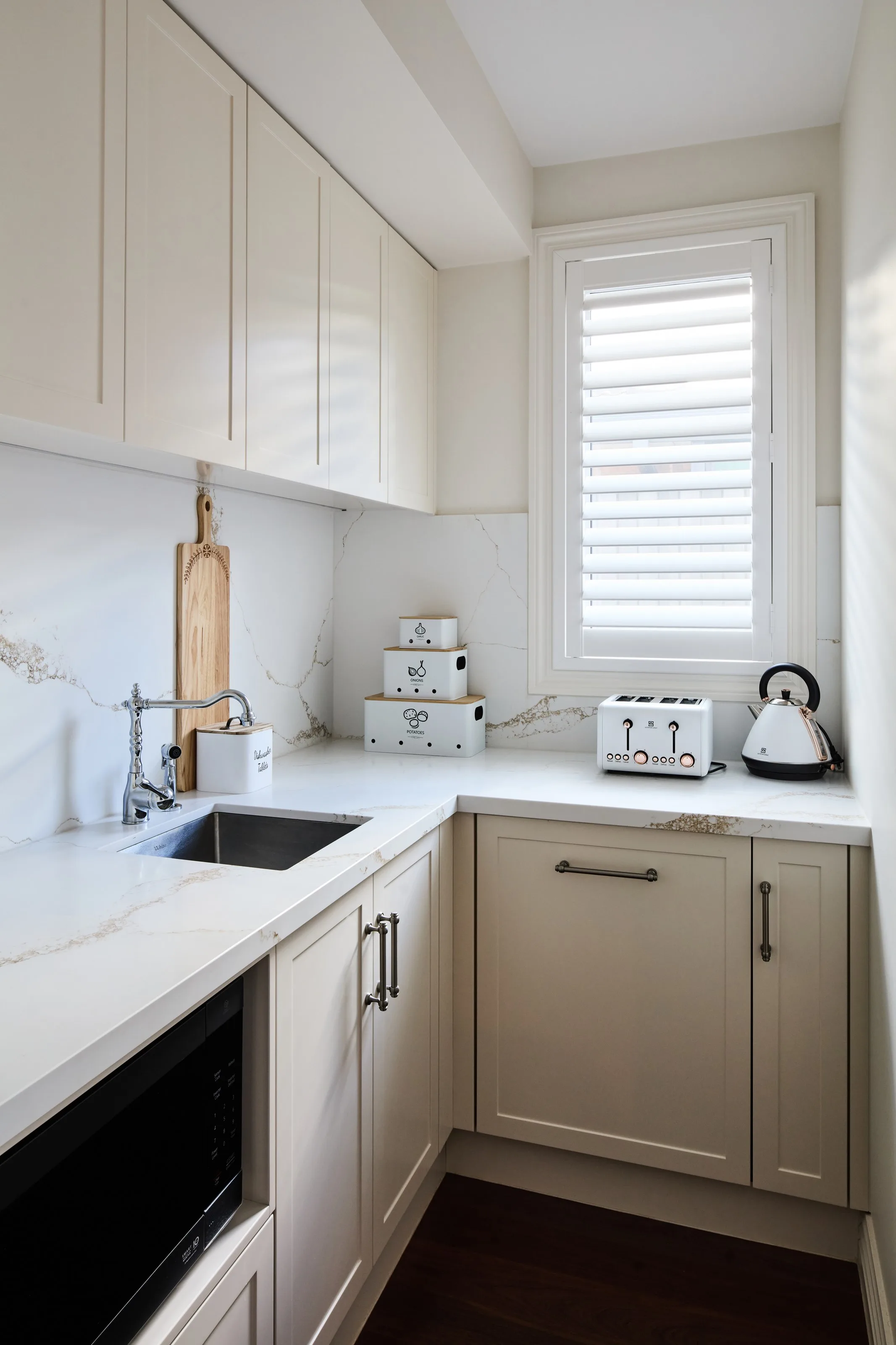 Butler&rsquo;s pantry in cream shaker joinery with a veined stone splashback and plantation shutters