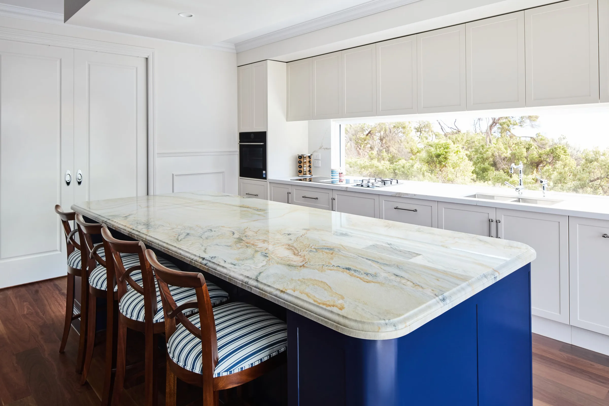 Patterned stone benchtop on the navy island, with the window splashback and wall oven beyond