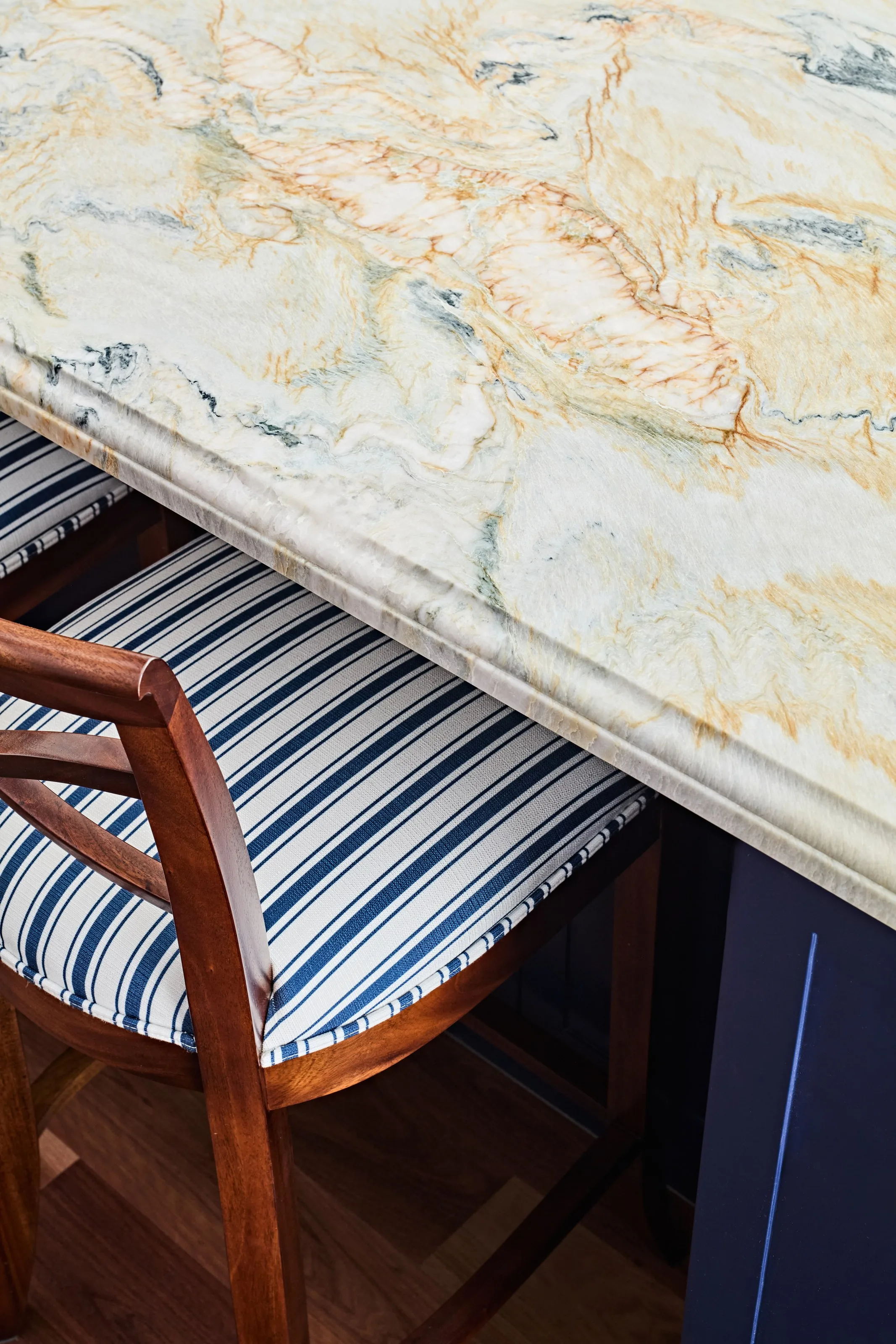 Detail of the marbled stone benchtop edge above a blue and white striped stool