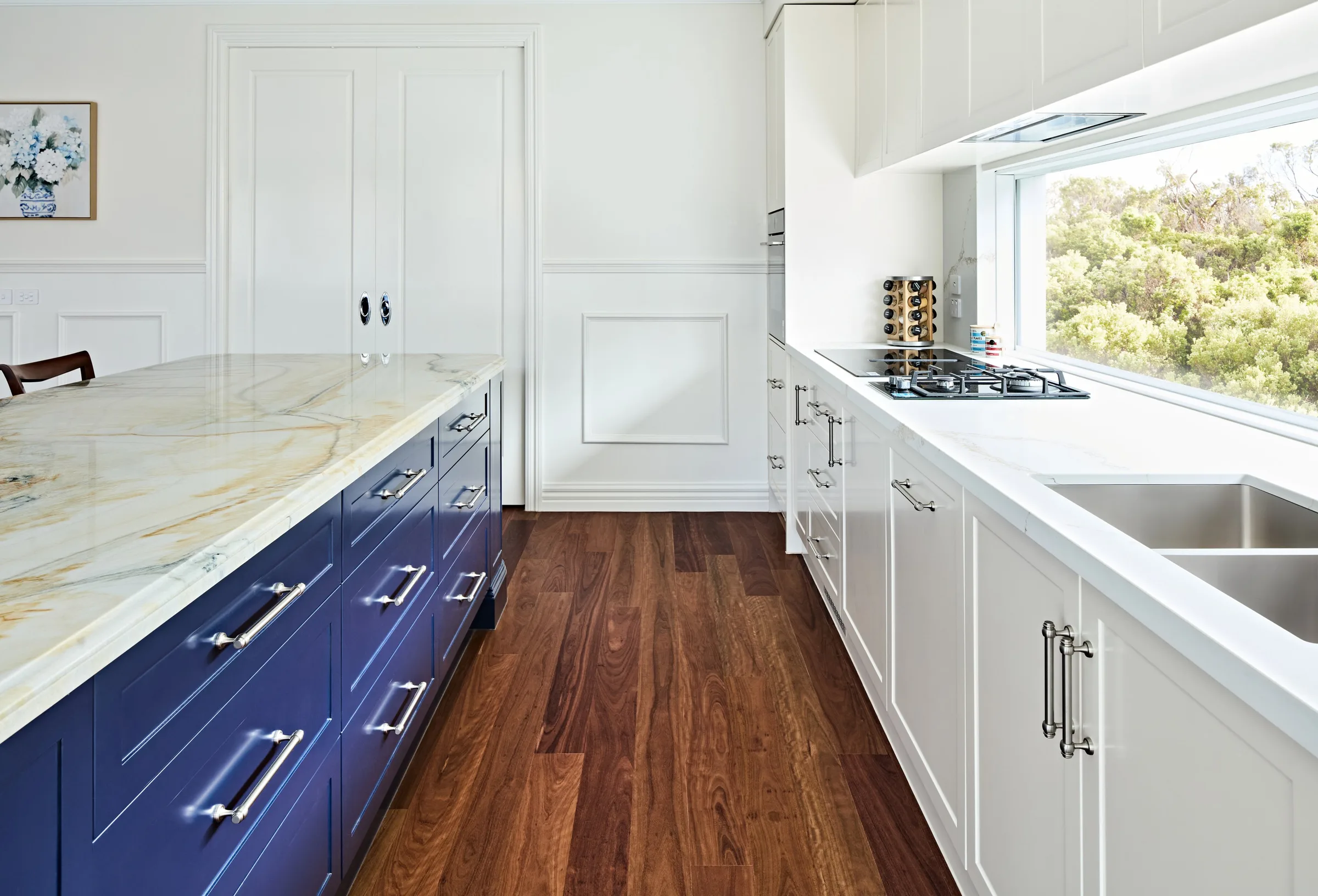 Looking down the kitchen: gas cooktop, window splashback and panelled joinery beside the navy island