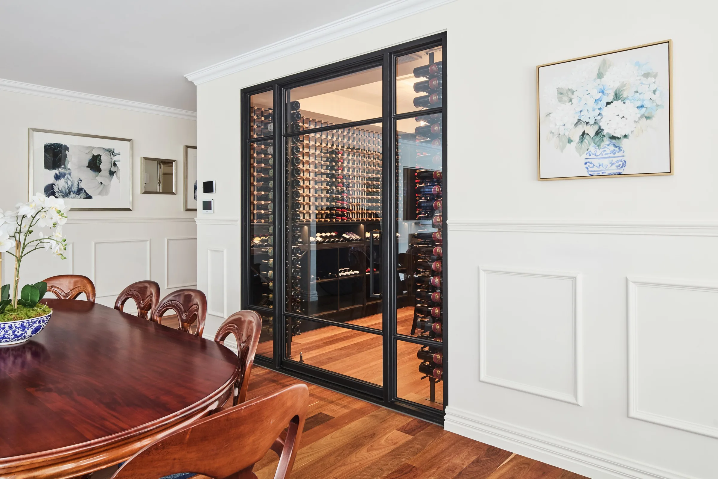 Formal dining room with wall panelling and a black-framed glazed wine cellar beyond