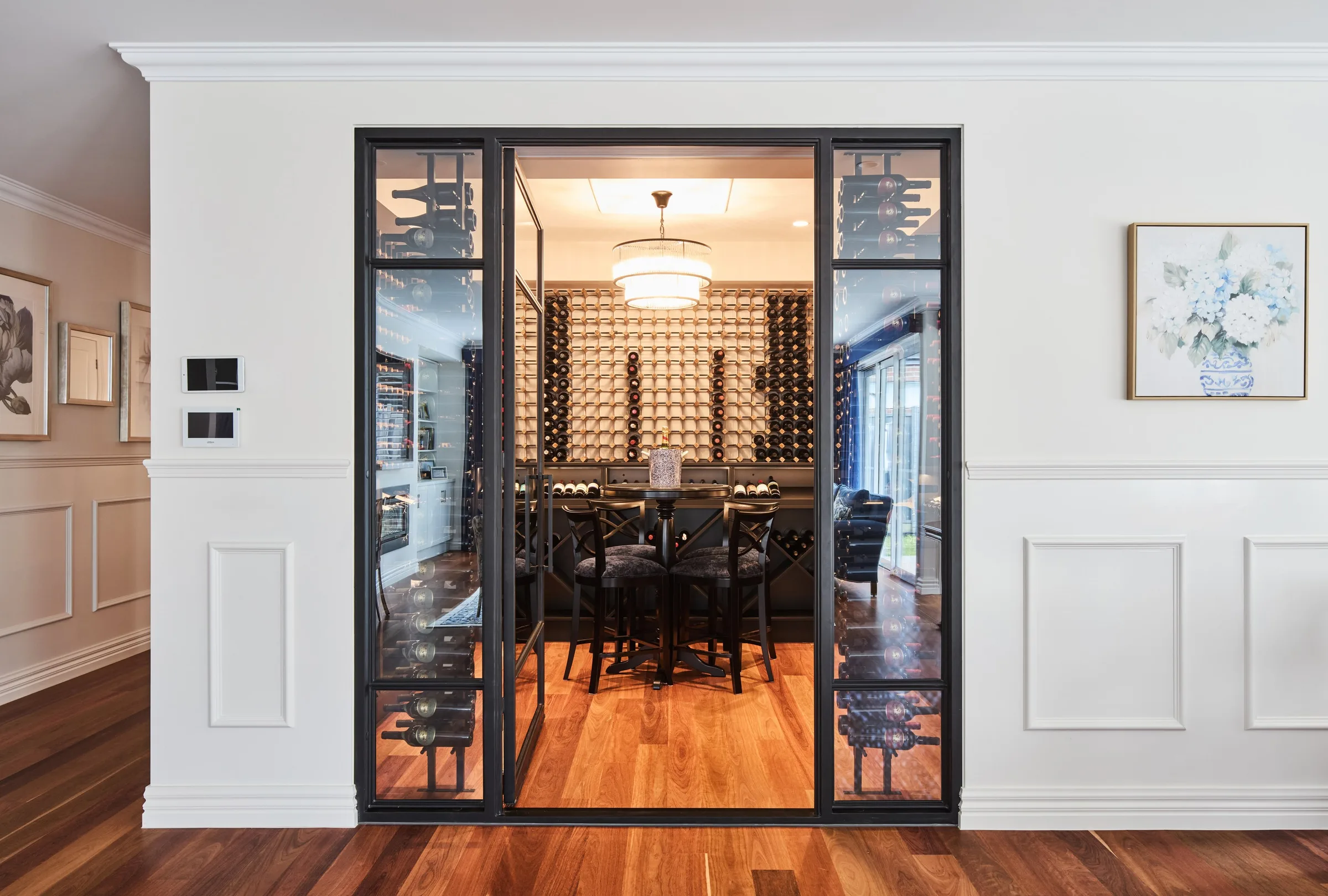 Steel-framed glass wine room set into the panelled wall, bottles racked around a tasting table