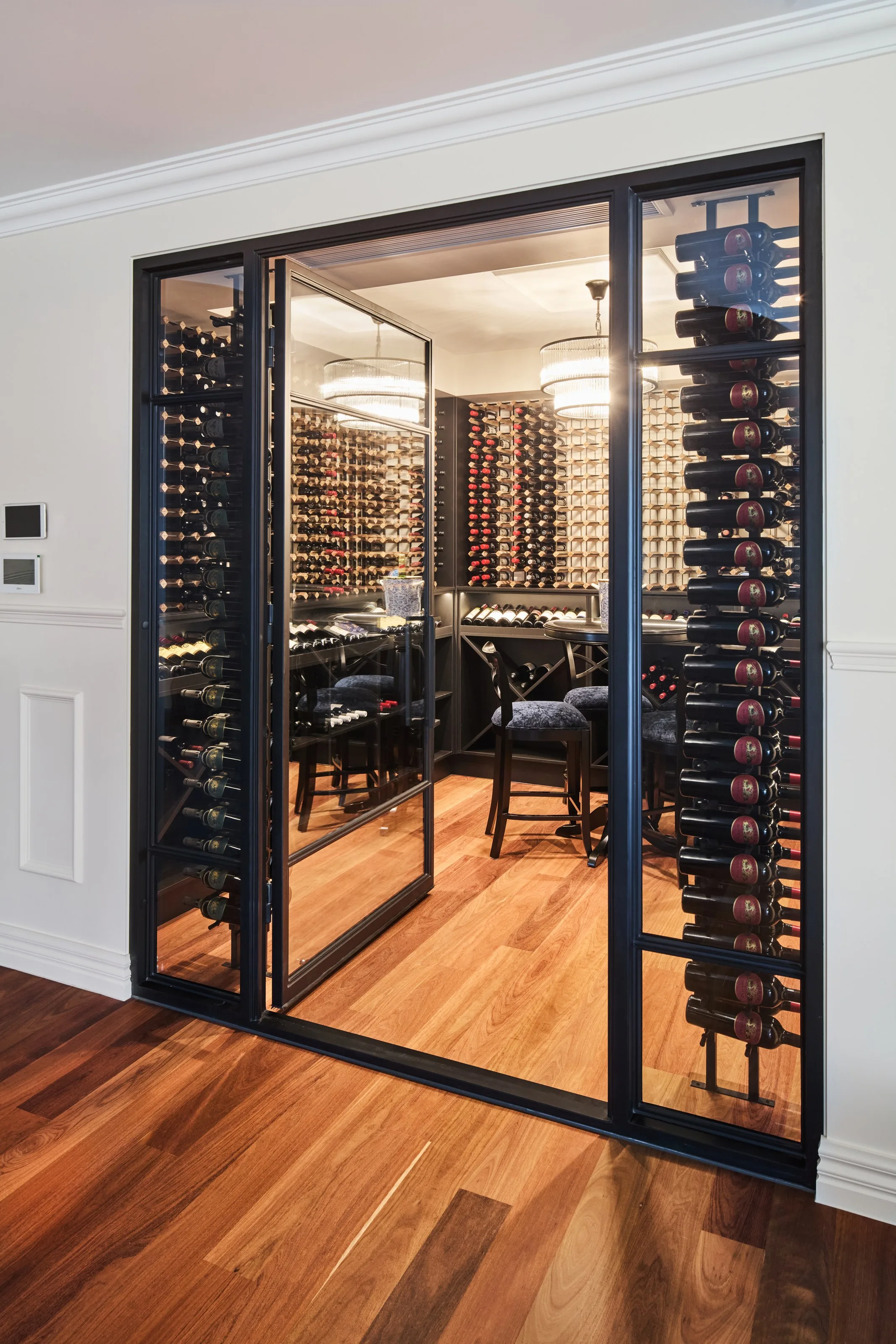 Glazed wine cellar viewed across timber floorboards, bottles displayed in the flanking racks