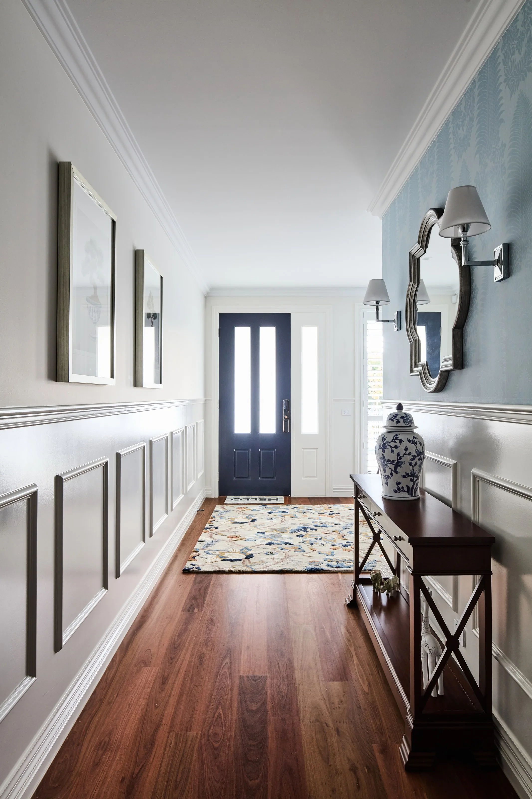 Entry hall with panelled wainscoting, a navy front door and a timber console beneath a mirror