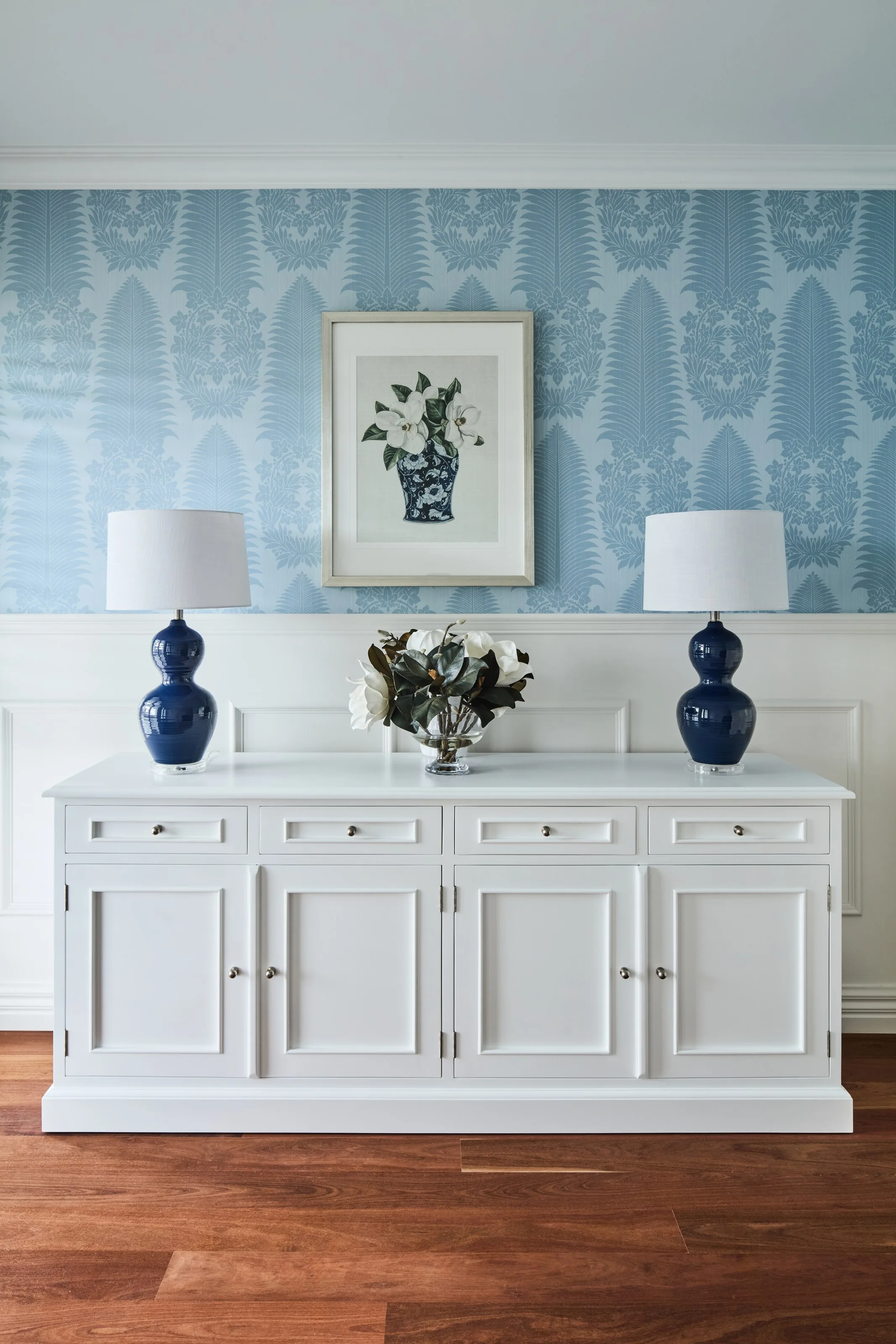 White sideboard against blue patterned wallpaper, flanked by a pair of navy table lamps