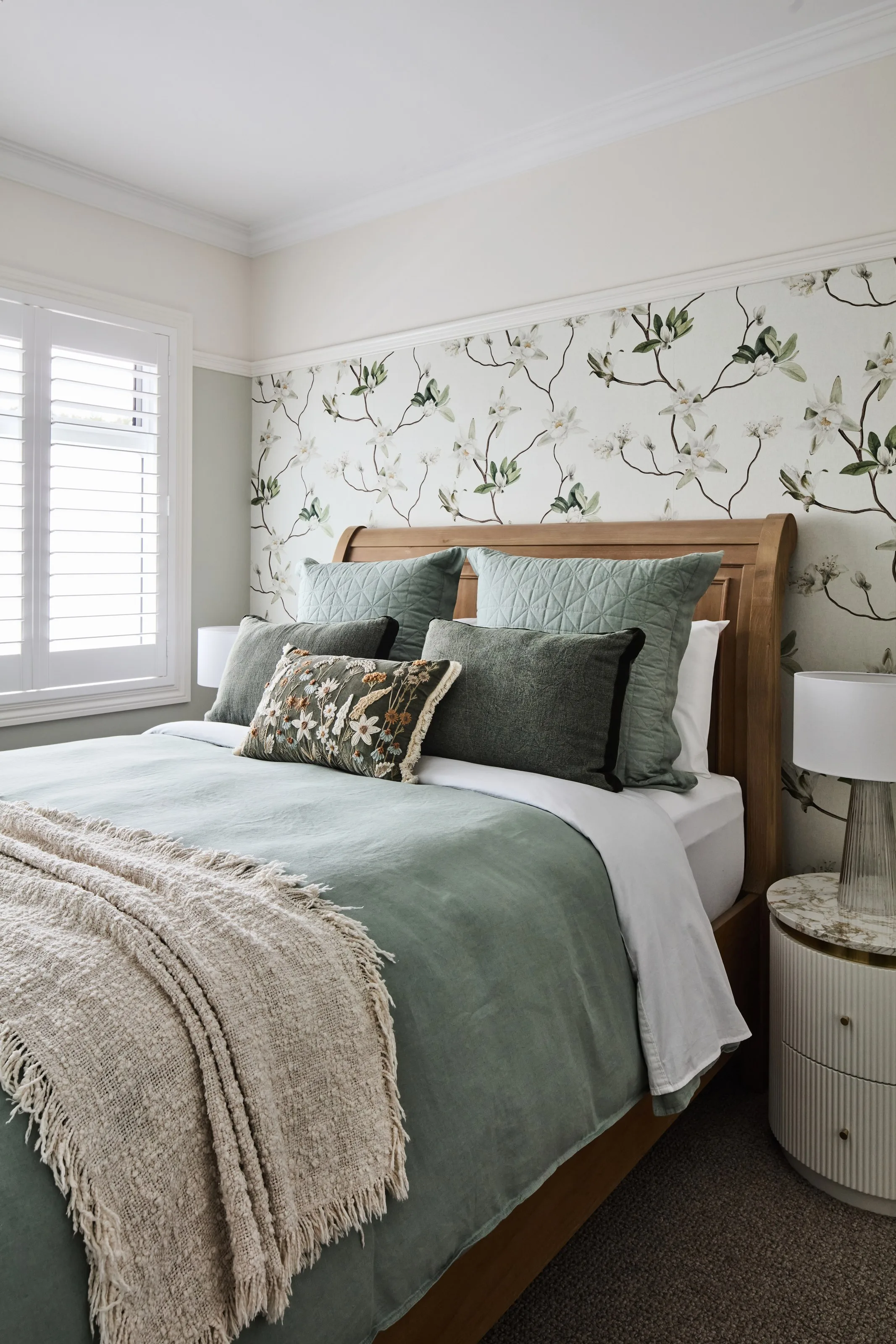 Bedroom with a curved timber bedhead, sage green bedding and floral wallpaper behind
