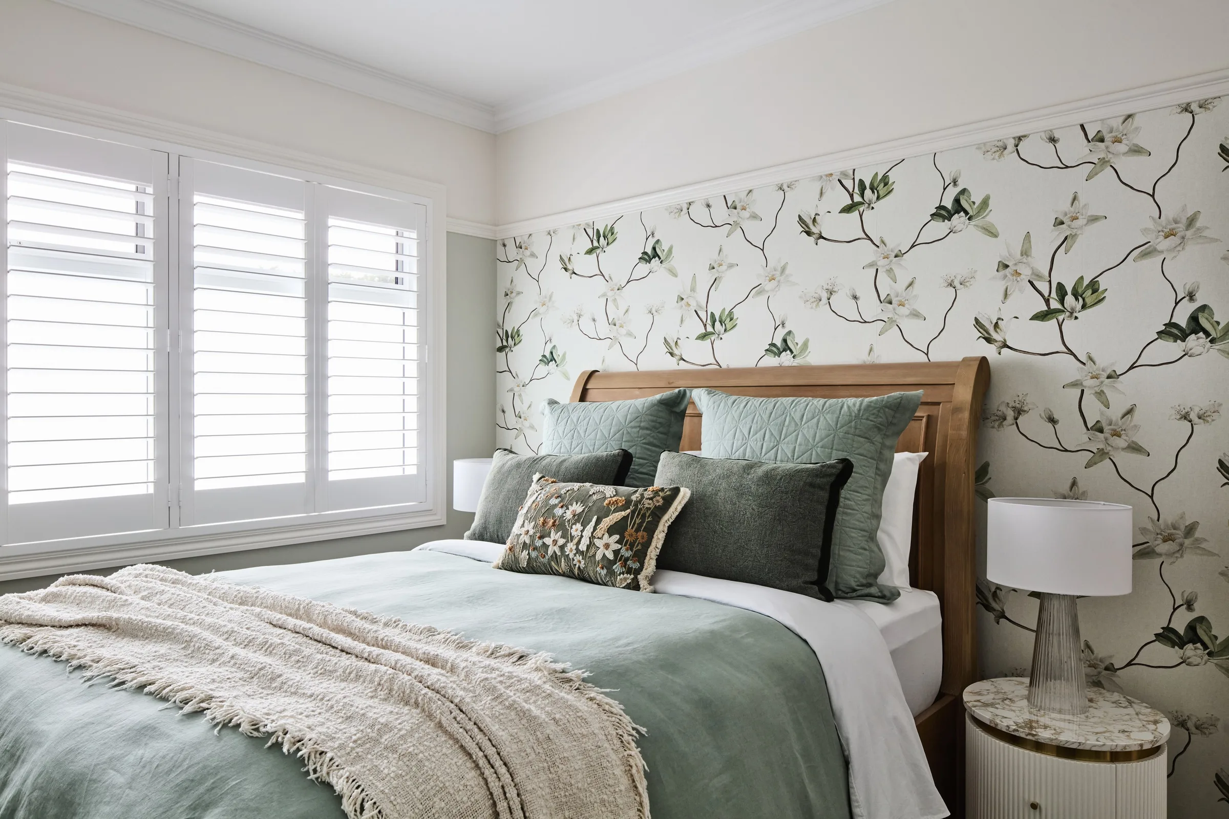 Bedroom seen from the side, plantation shutters throwing light across layered green linen