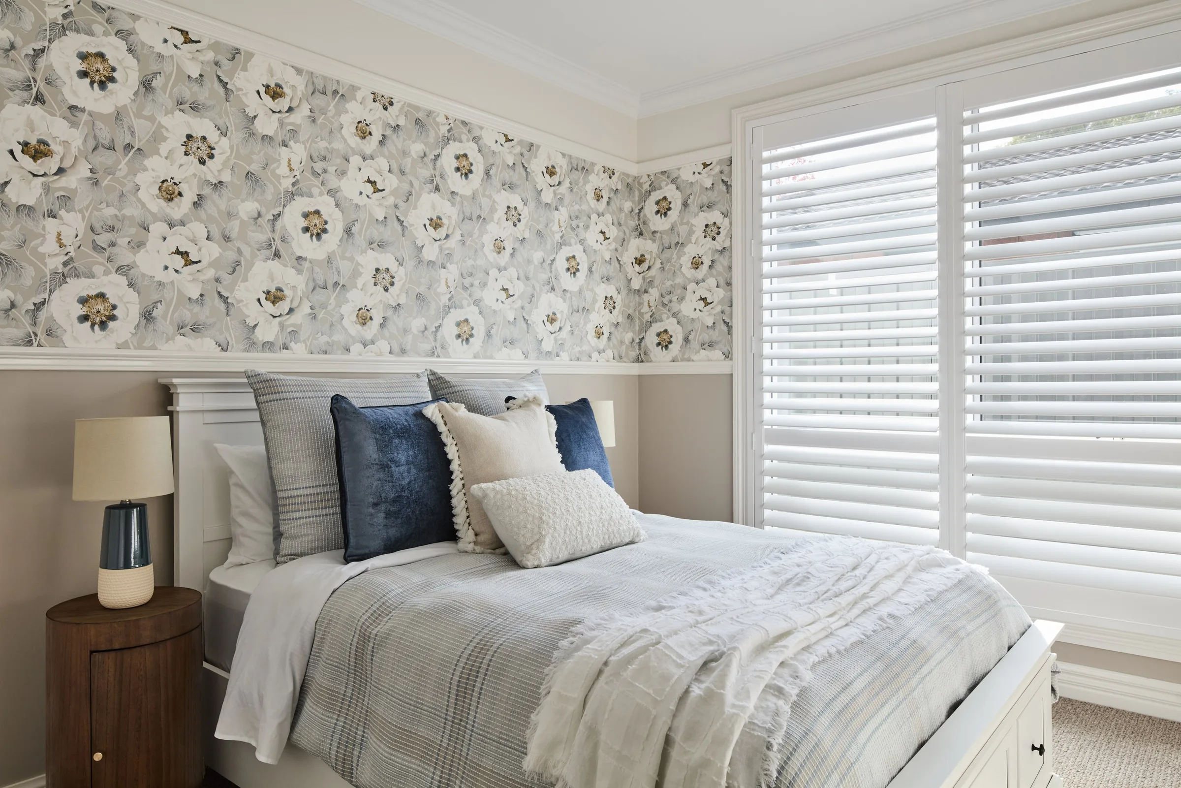Second bedroom with grey floral wallpaper, white venetian blinds and navy cushions on pale bedding