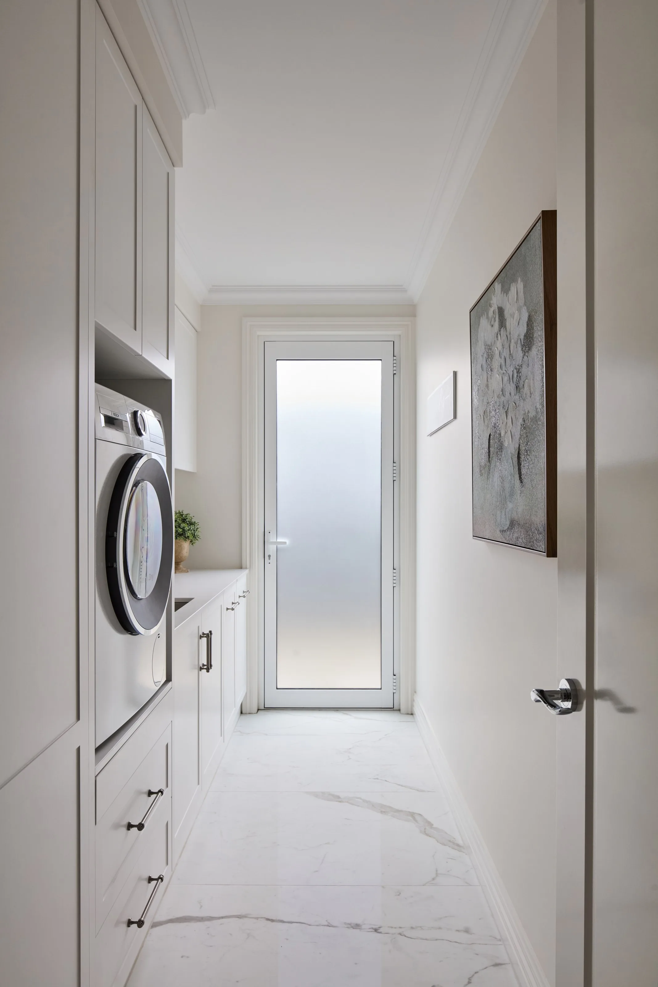 Laundry in cream joinery with a stacked washer and dryer and marble-look tiles to the external door