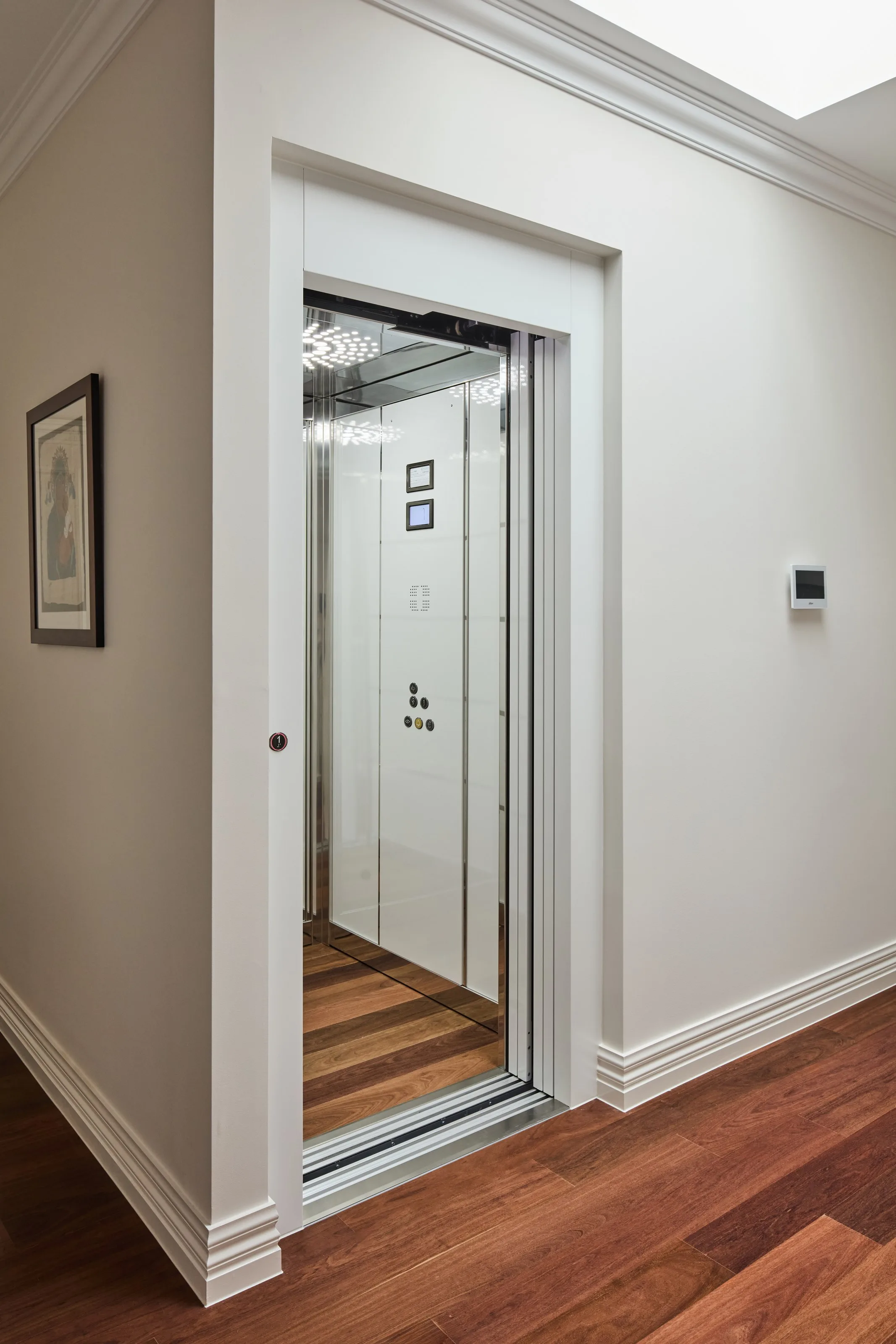 Residential lift standing open, mirrored car interior and timber-lined floor