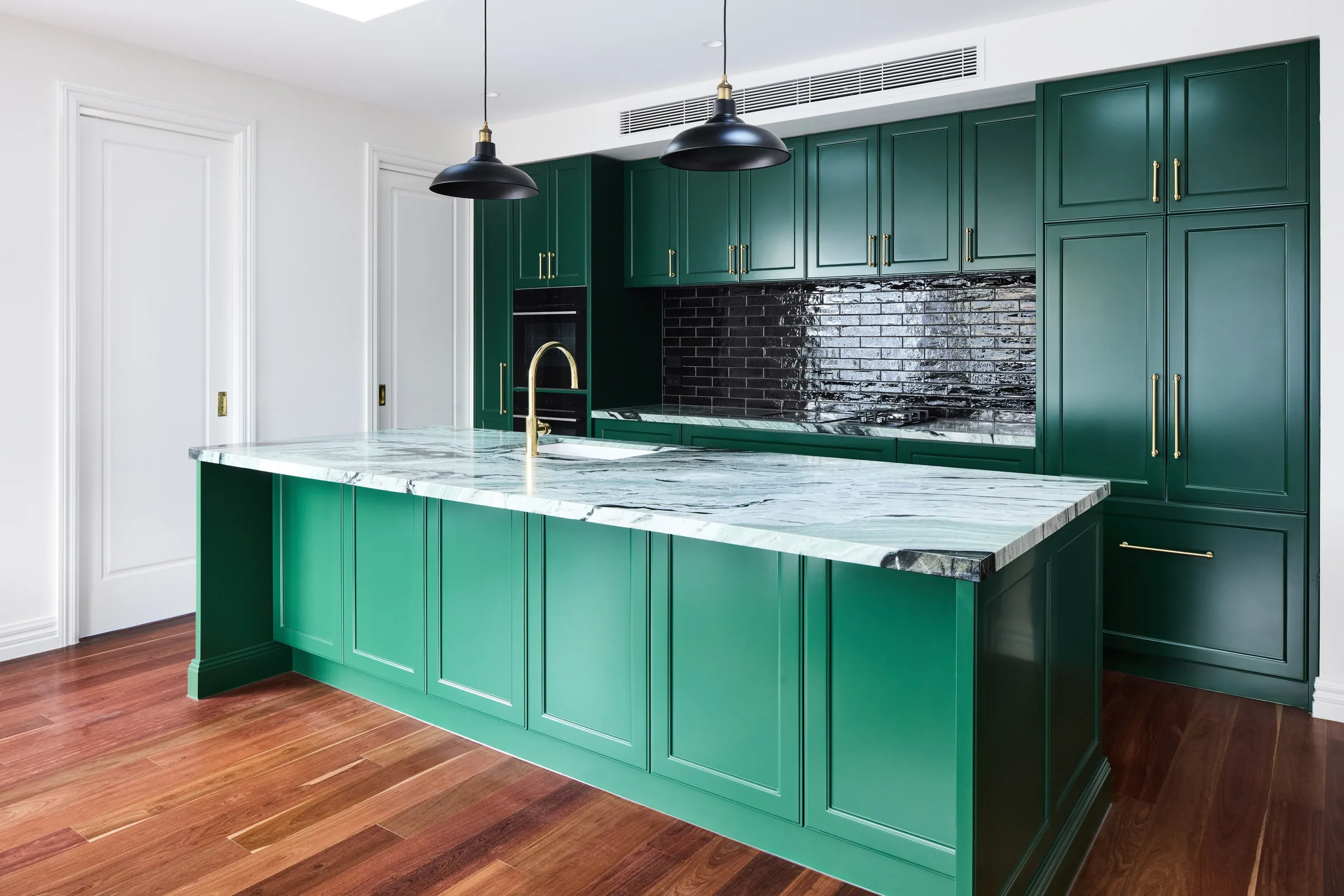 Green marble island benchtop running the length of a deep green kitchen, timber floors underfoot