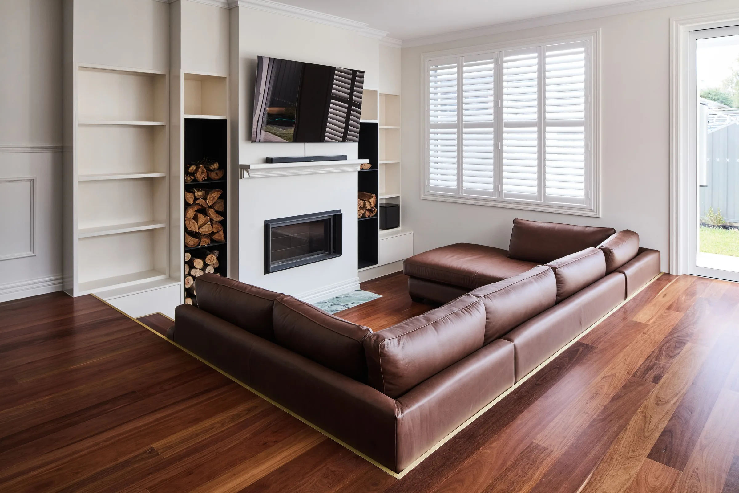 Living room in the second home with a brown leather modular lounge, gas fireplace and built-in firewood storage