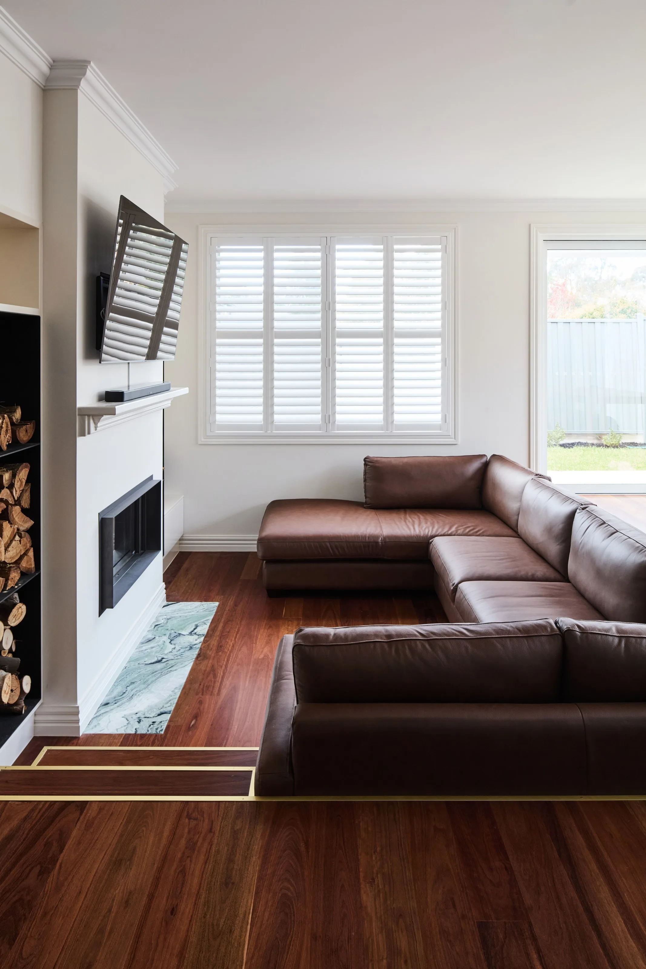 Plantation shutters and a white fireplace surround beside a leather lounge on timber floors
