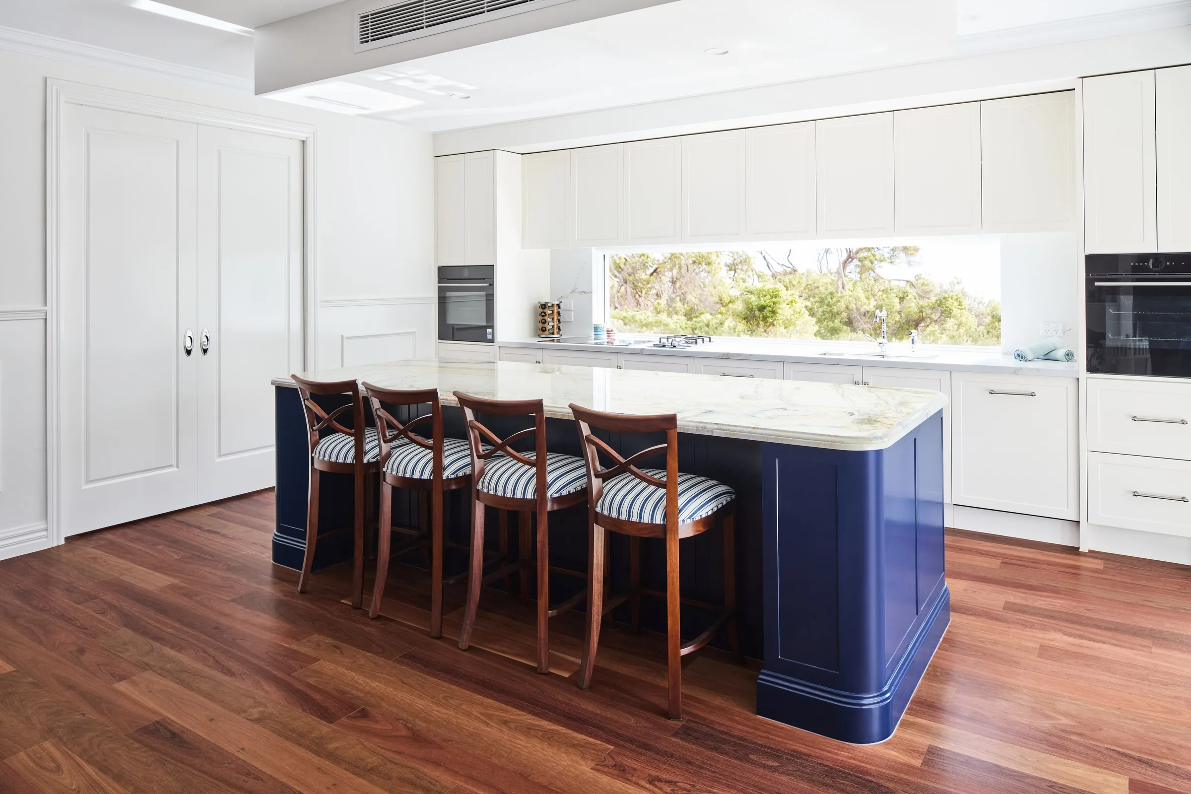 Navy shaker island with striped bar stools in the white kitchen of the main home at Thom St