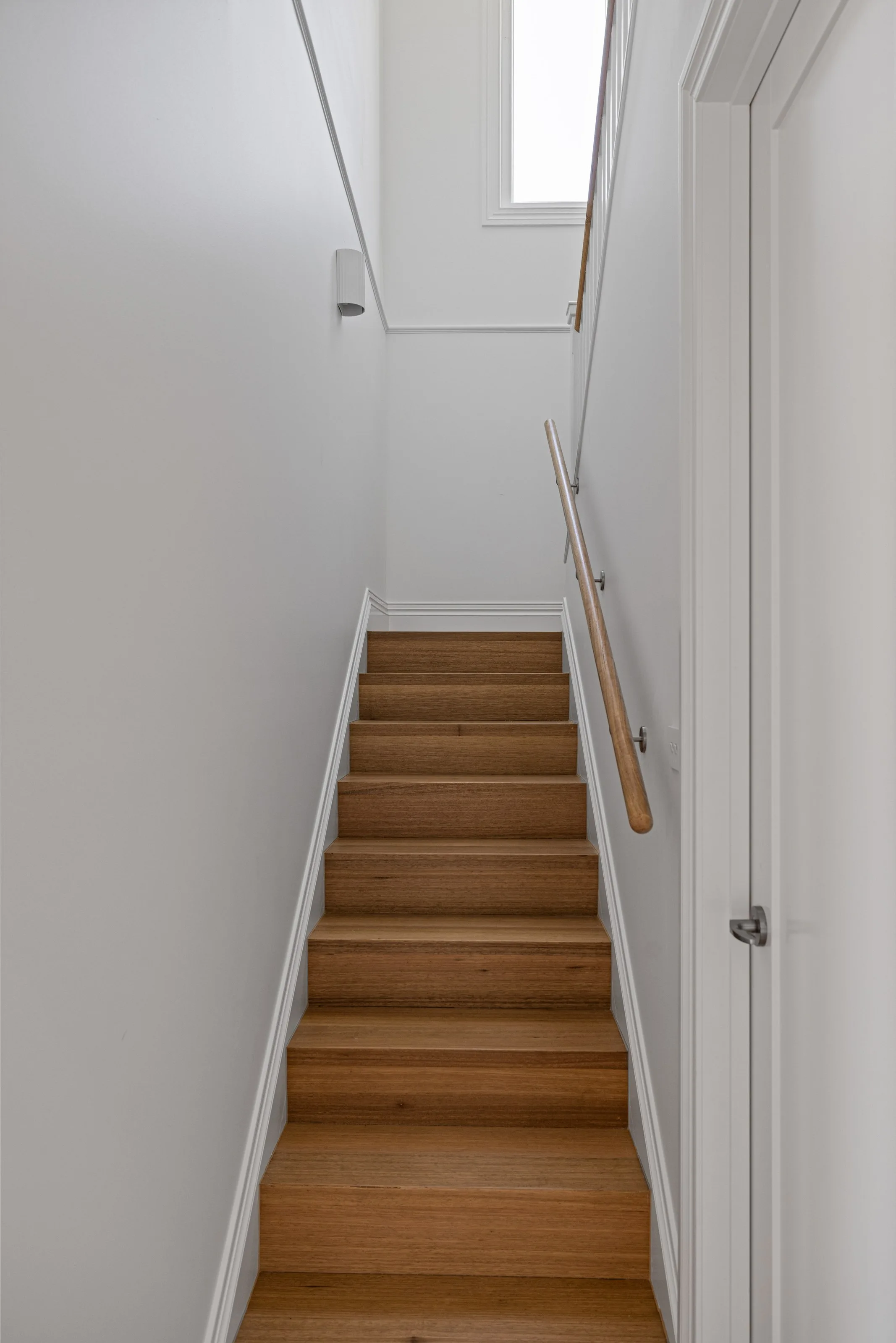 Narrow staircase with oak treads, white walls and a slim timber handrail rising to a landing window