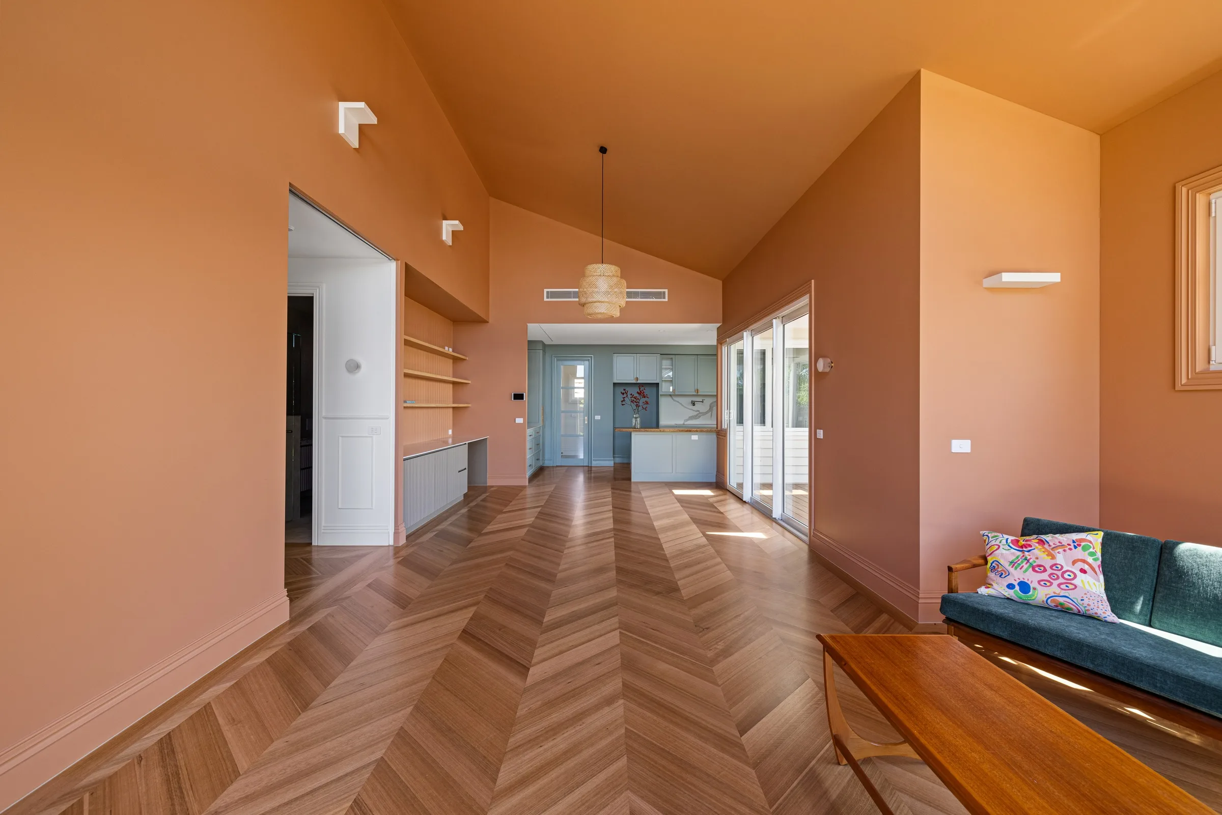 Terracotta walls and a woven pendant over chevron parquet, with a green velvet sofa and timber coffee table