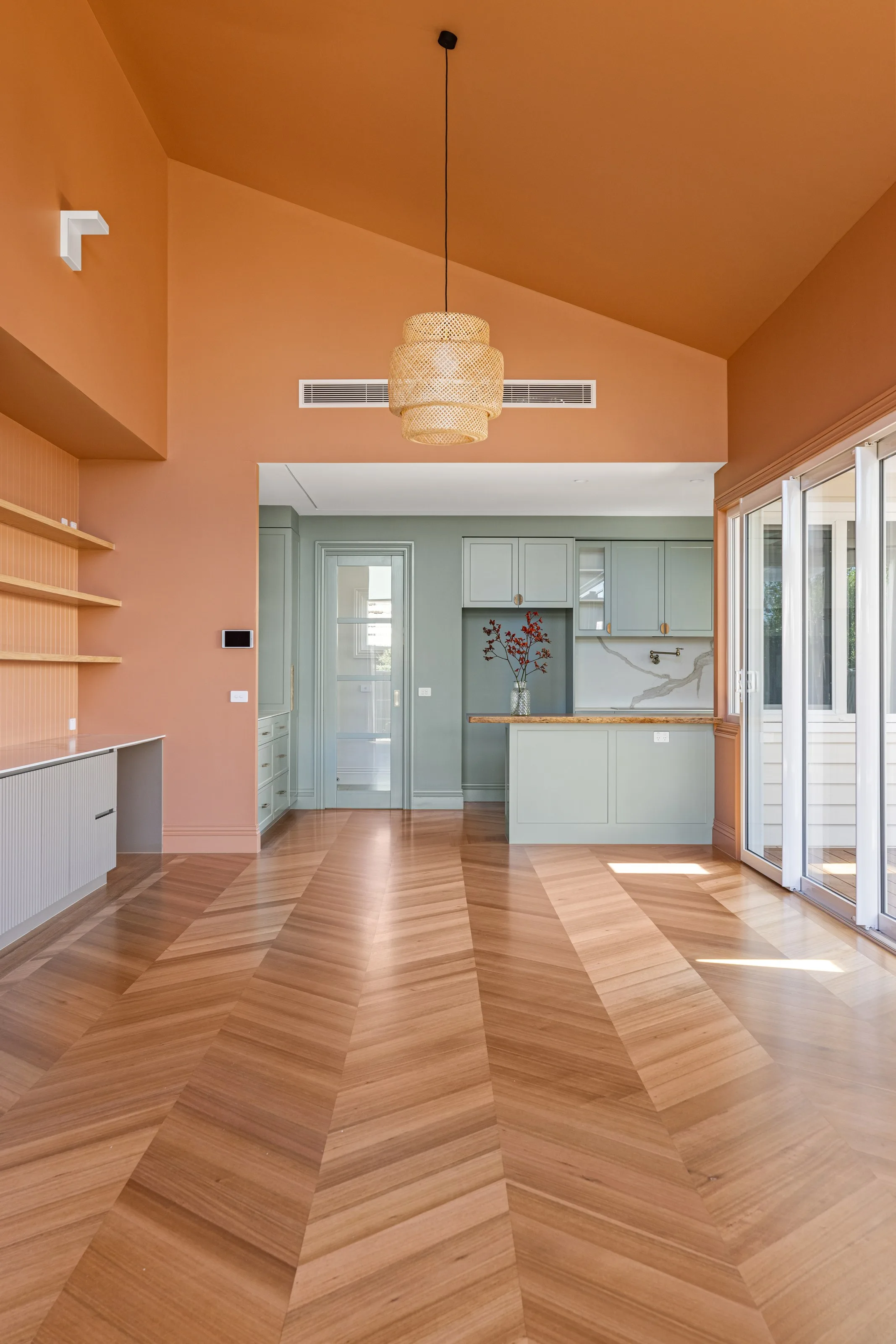 Raked terracotta ceiling and woven rattan pendant above chevron parquet, glazed doors to the right